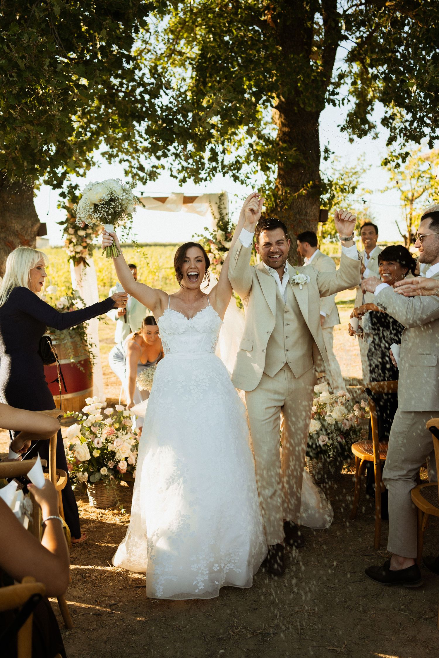 Joyful bride and groom walk down the aisle as guests toss rice at their outdoor wedding ceremony.