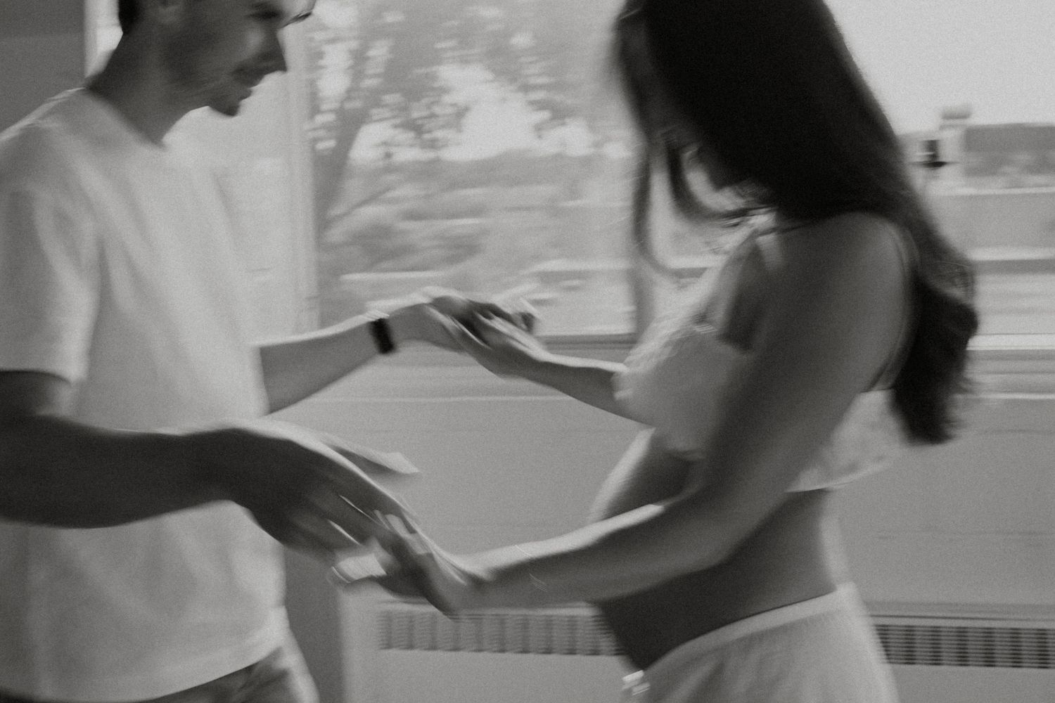 Black and white photo of a man and woman exchanging items indoors near a window.