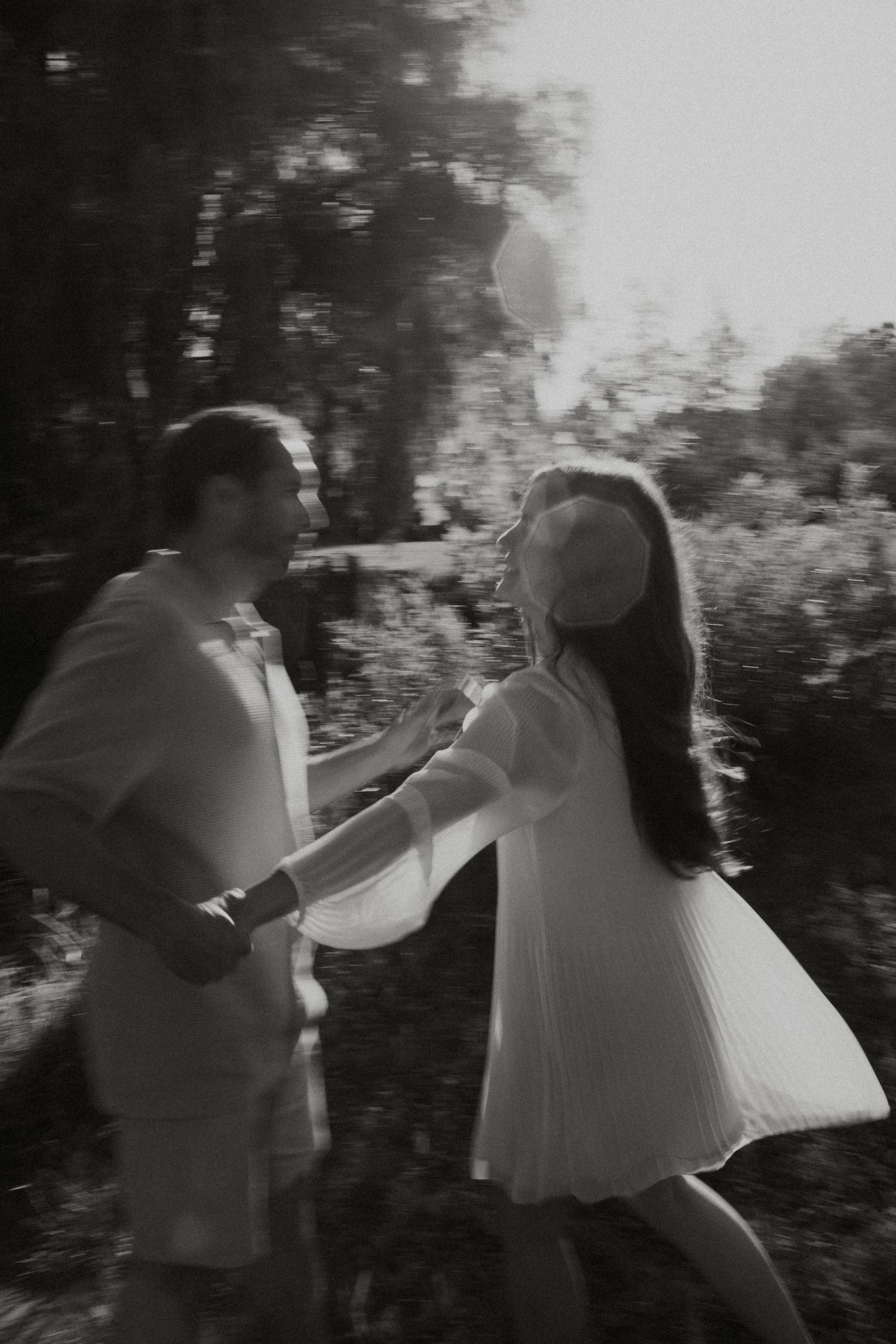 Black and white photo of a couple dancing together outdoors in a garden, captured with a dreamy motion blur effect.