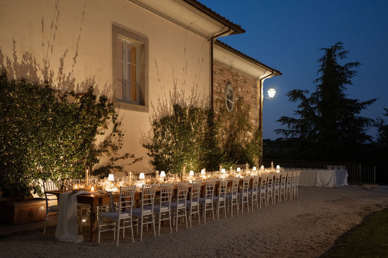Elegant outdoor dinner party at a Tuscan villa at dusk, long table set with candles and glassware.