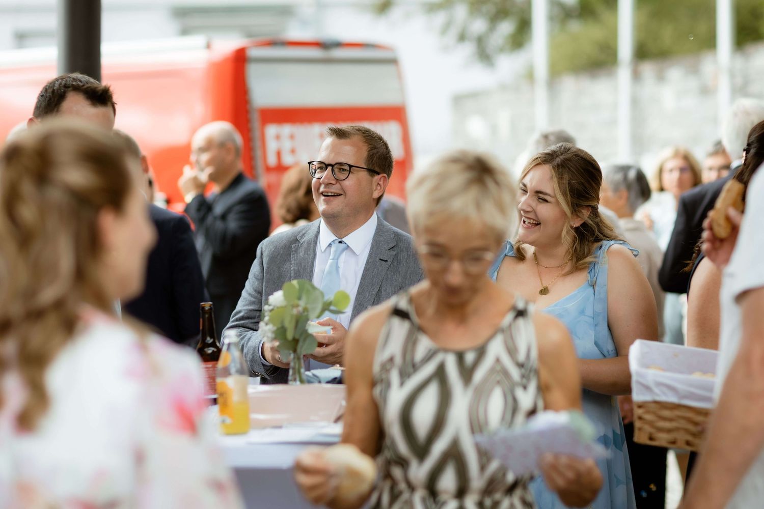 Guests smiling and socializing at an outdoor event with a red food truck in the background on a sunny day.