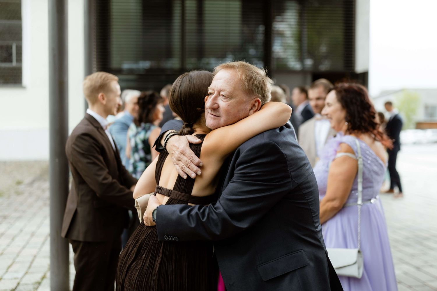 Two wedding guests share a warm embrace outside the ceremony venue.