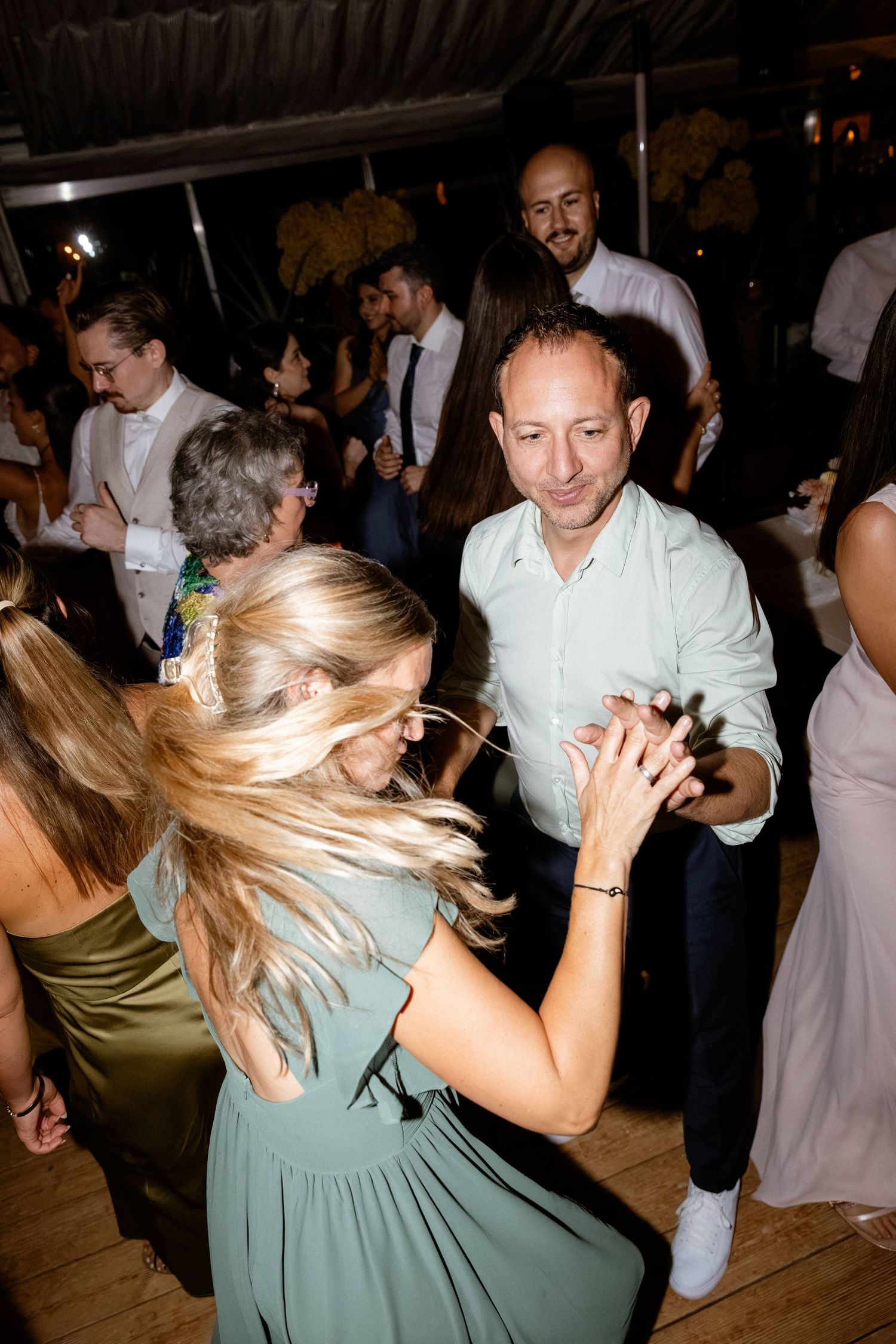 Couple dancing energetically at a wedding reception on a wooden dance floor.