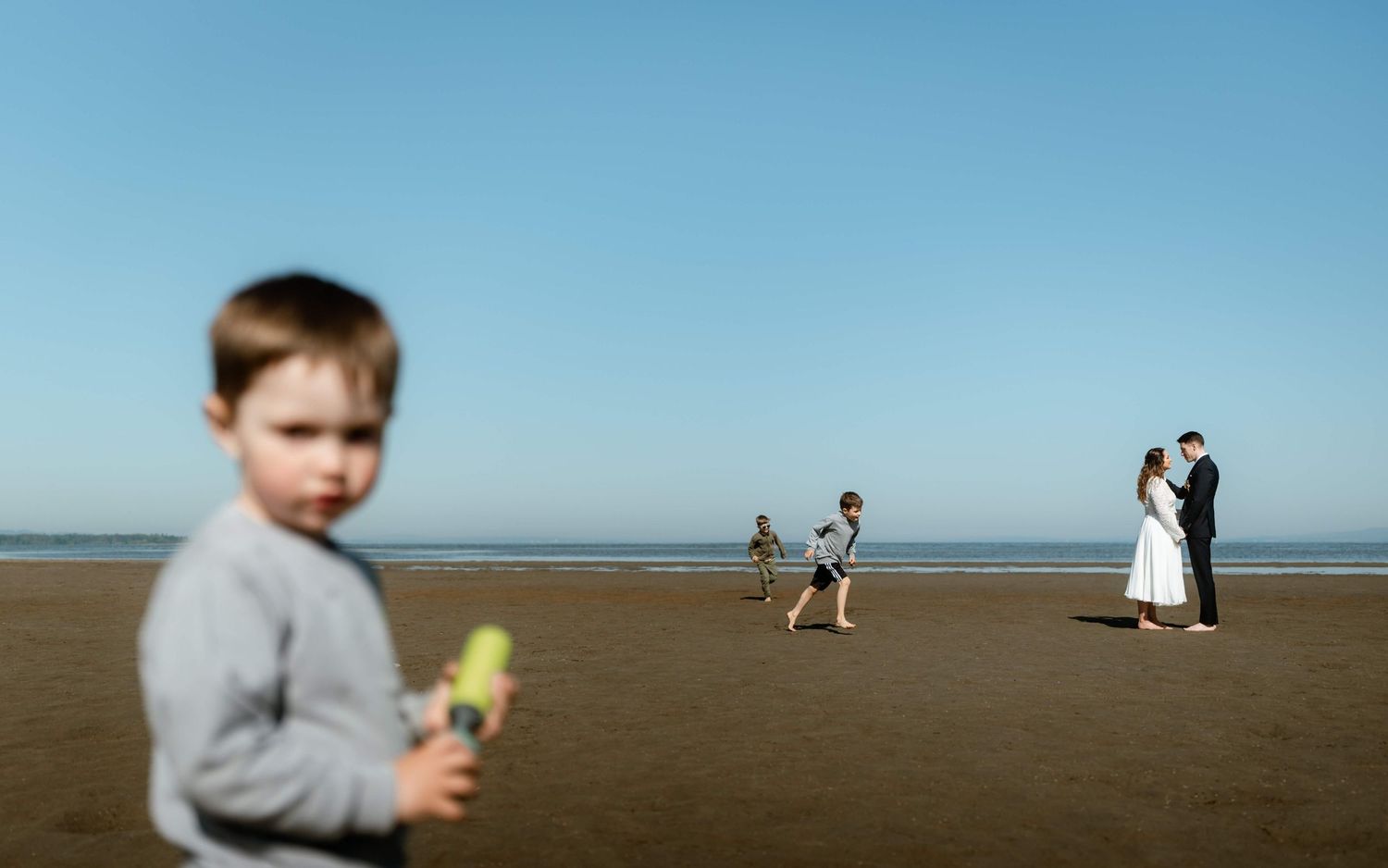 Child on beach foreground with wedding couple embracing in background.