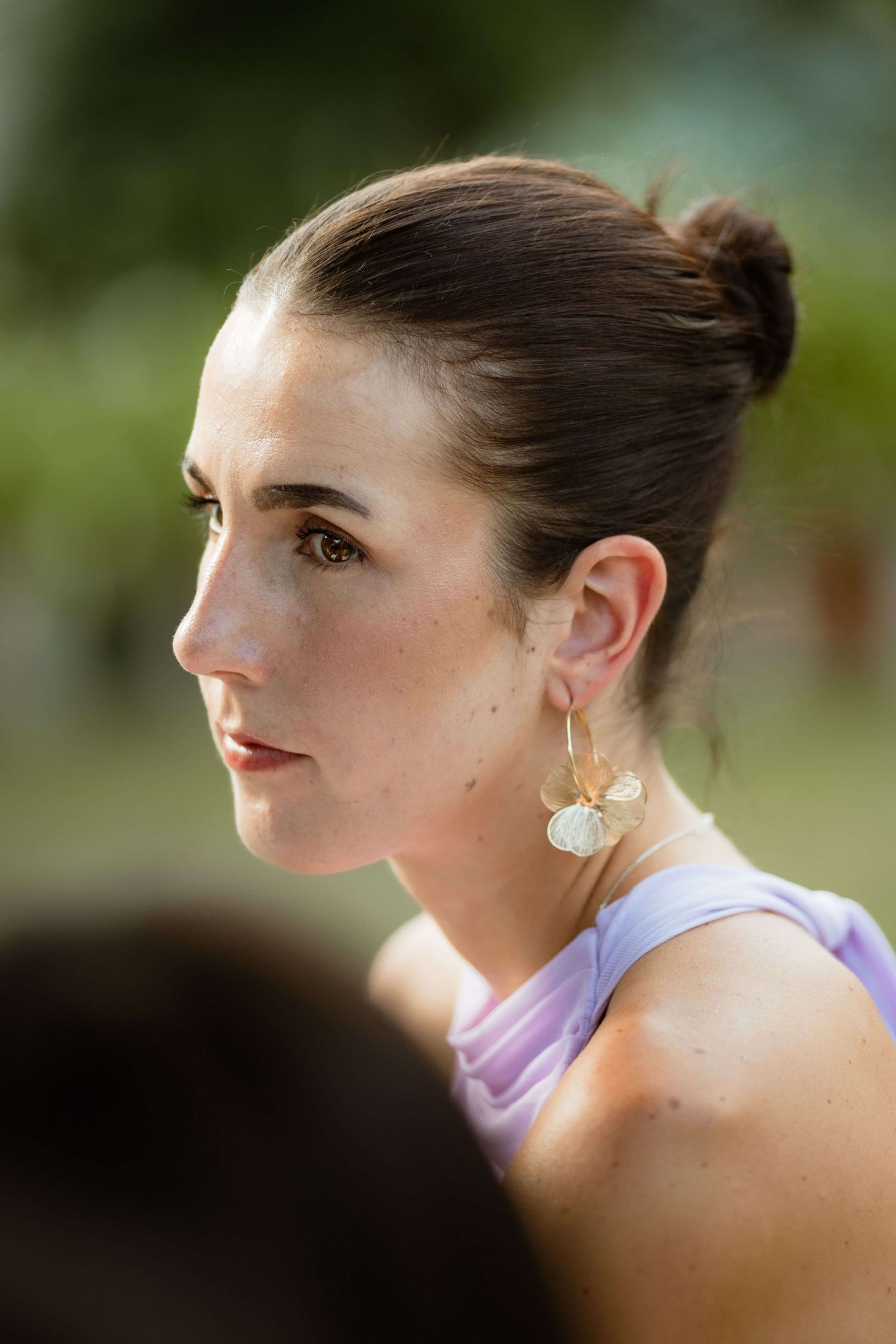 Elegant wedding guest with updo hairstyle and gold earrings at outdoor ceremony.