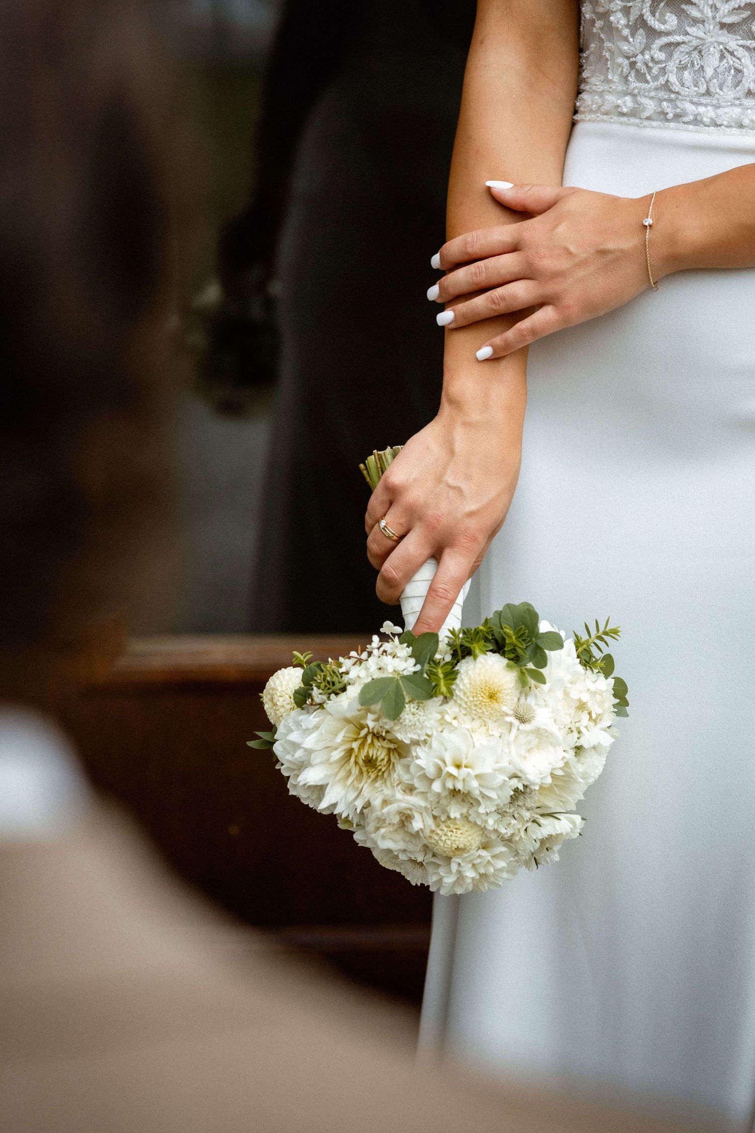 Bride in white lace gown holding an elegant white dahlia and eucalyptus wedding bouquet.