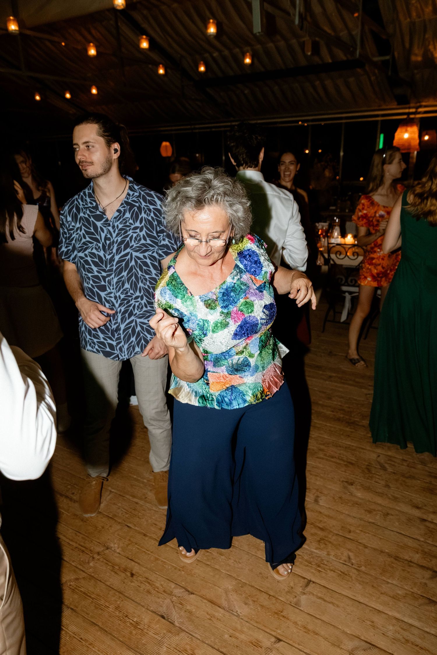 Elderly woman dancing joyfully with a young man at a wedding reception.