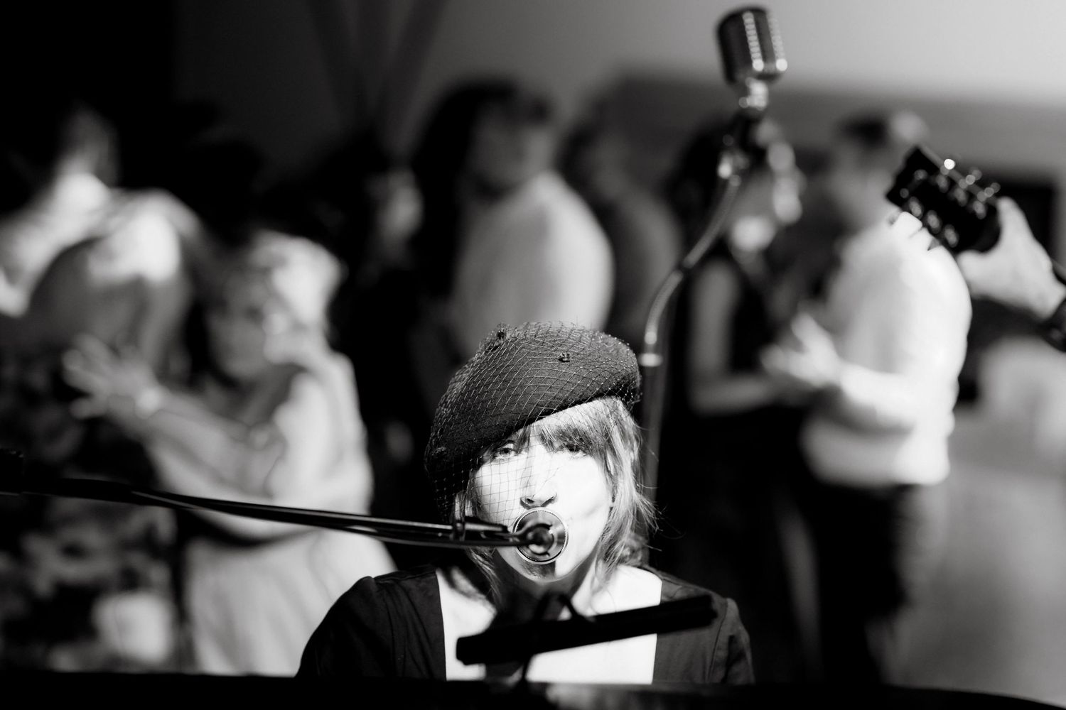 Black and white photo of a young musician wearing a beret performing at a live wedding reception.