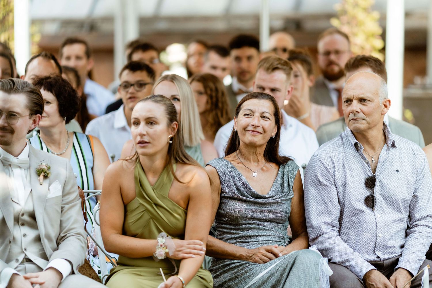 Wedding guests seated outdoors, smiling and watching the ceremony on a sunny day.