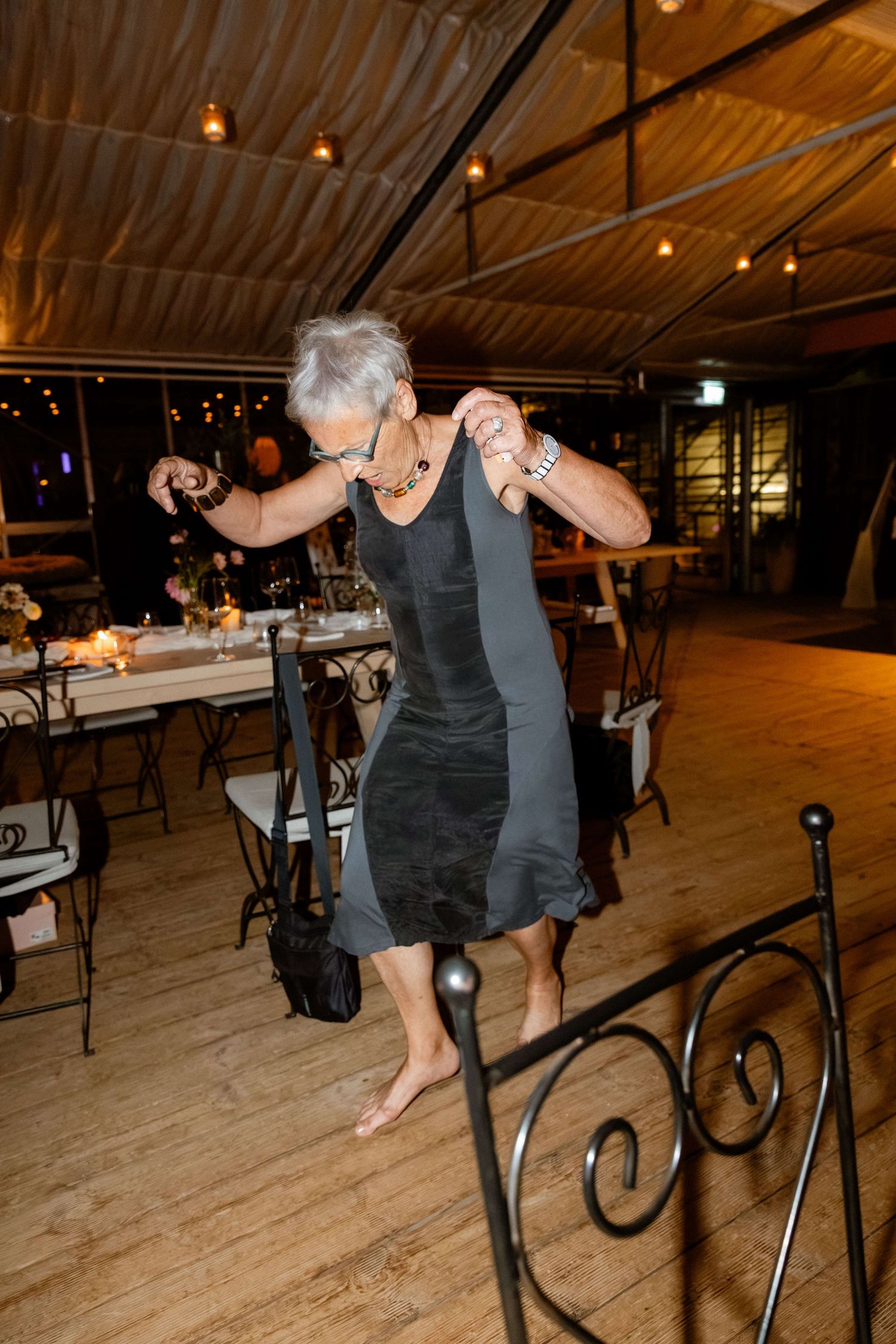Older woman dancing barefoot alone on a wooden floor at a wedding.