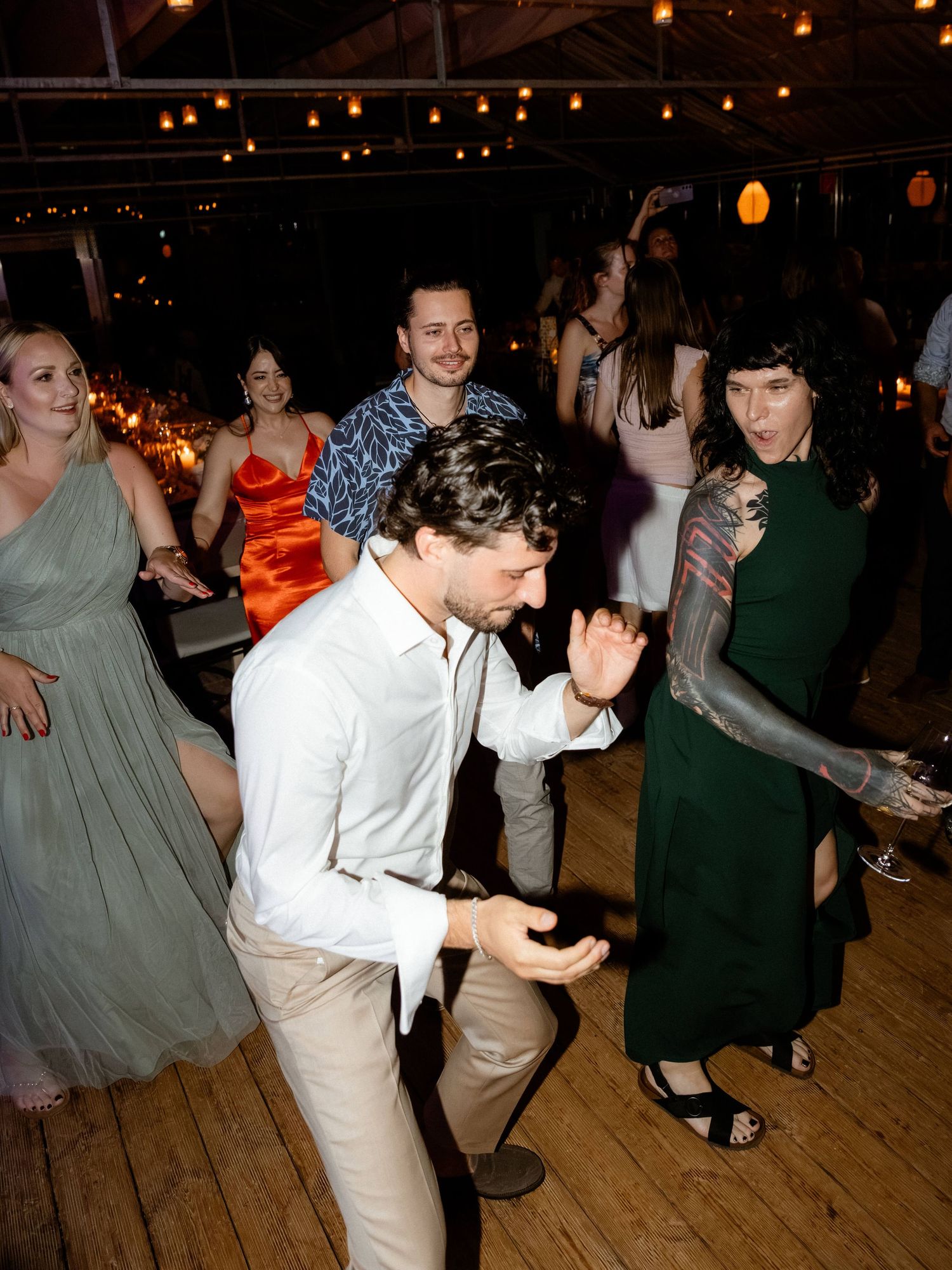 Guests dancing at wedding reception, woman in green dress and man in white shirt.