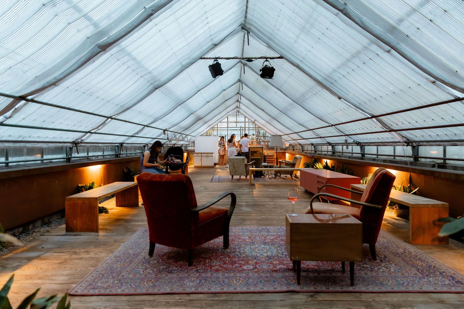 Cozy greenhouse wedding lounge with vintage armchairs and warm lighting under glass ceiling.