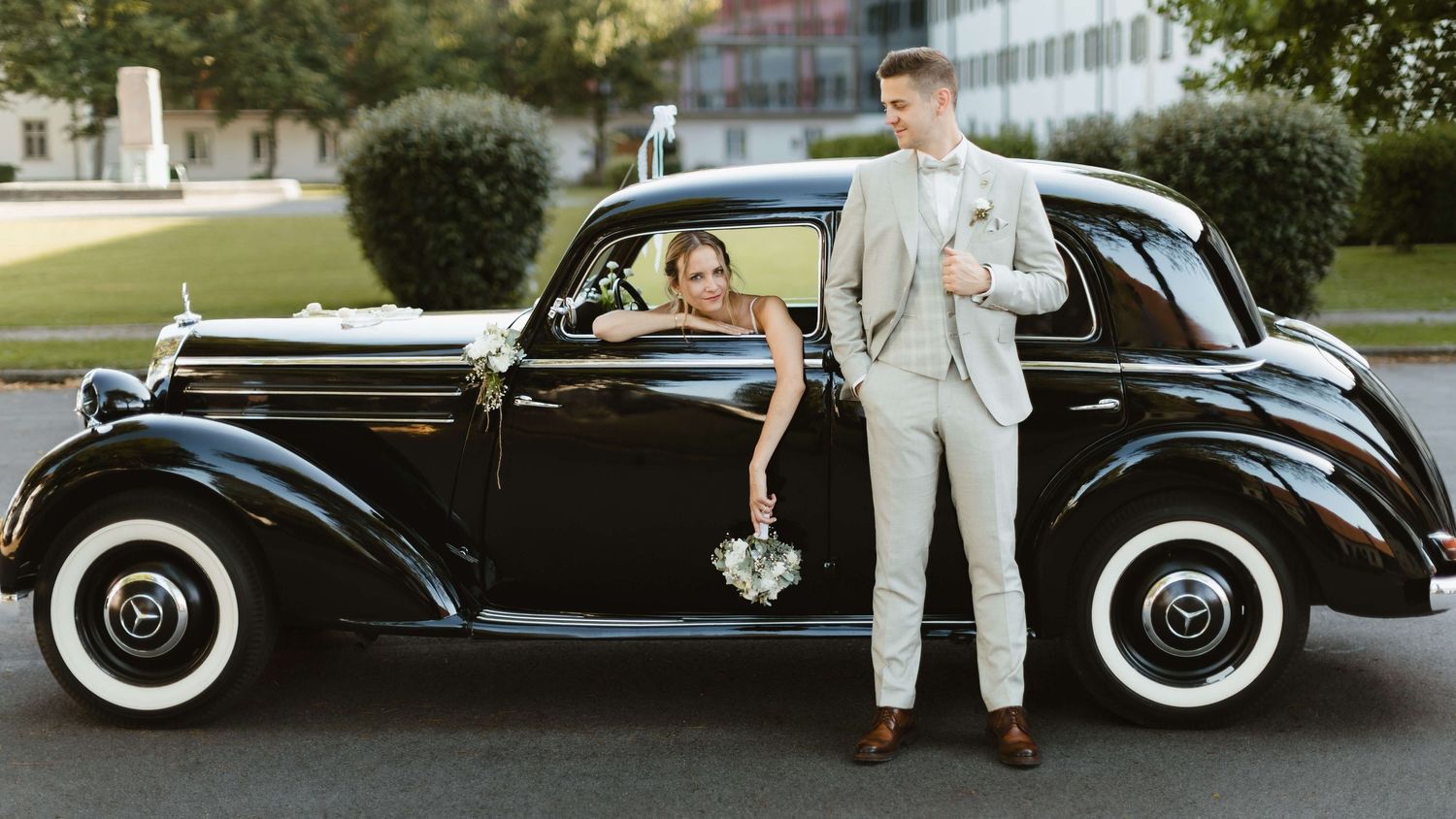 Wedding couple posing beside vintage black classic car outdoors.