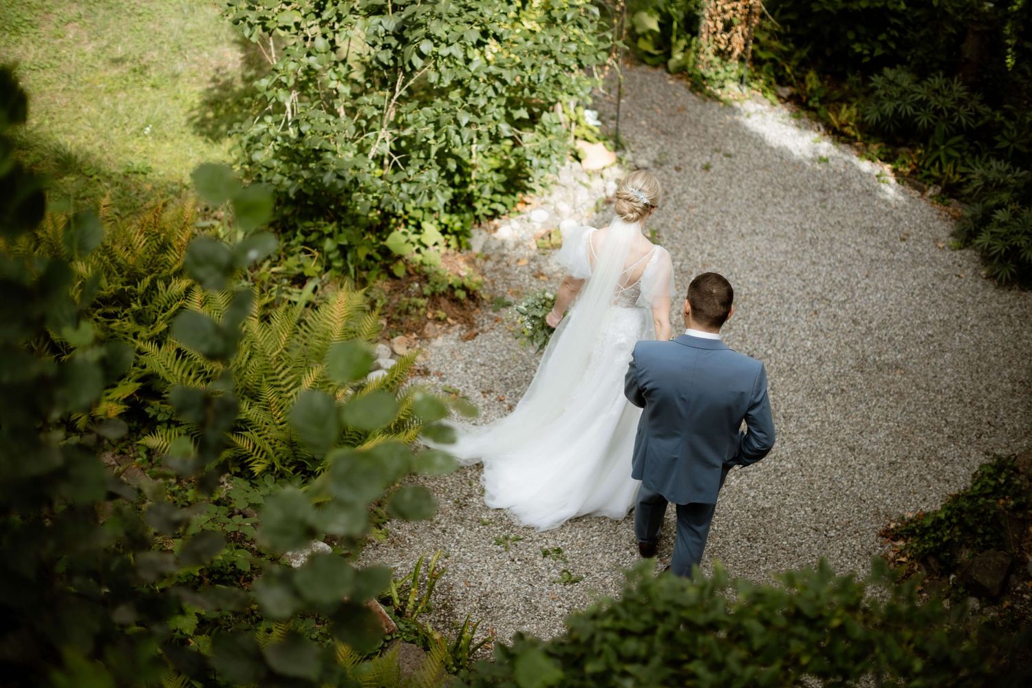 Aerial view of bride and groom walking together along a garden gravel path.
