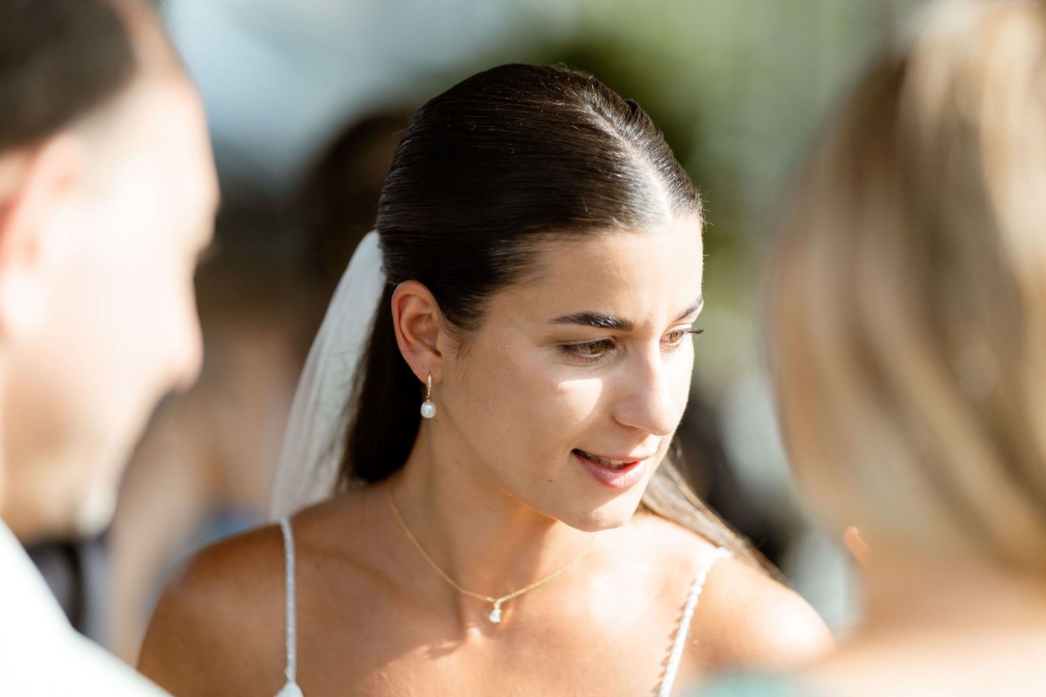 Bride in veil and pearl earrings smiling at wedding guests.
