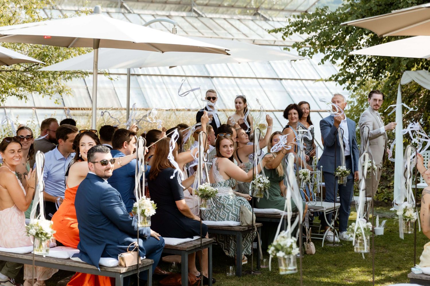 Wedding guests celebrating outdoor ceremony under large patio umbrellas.