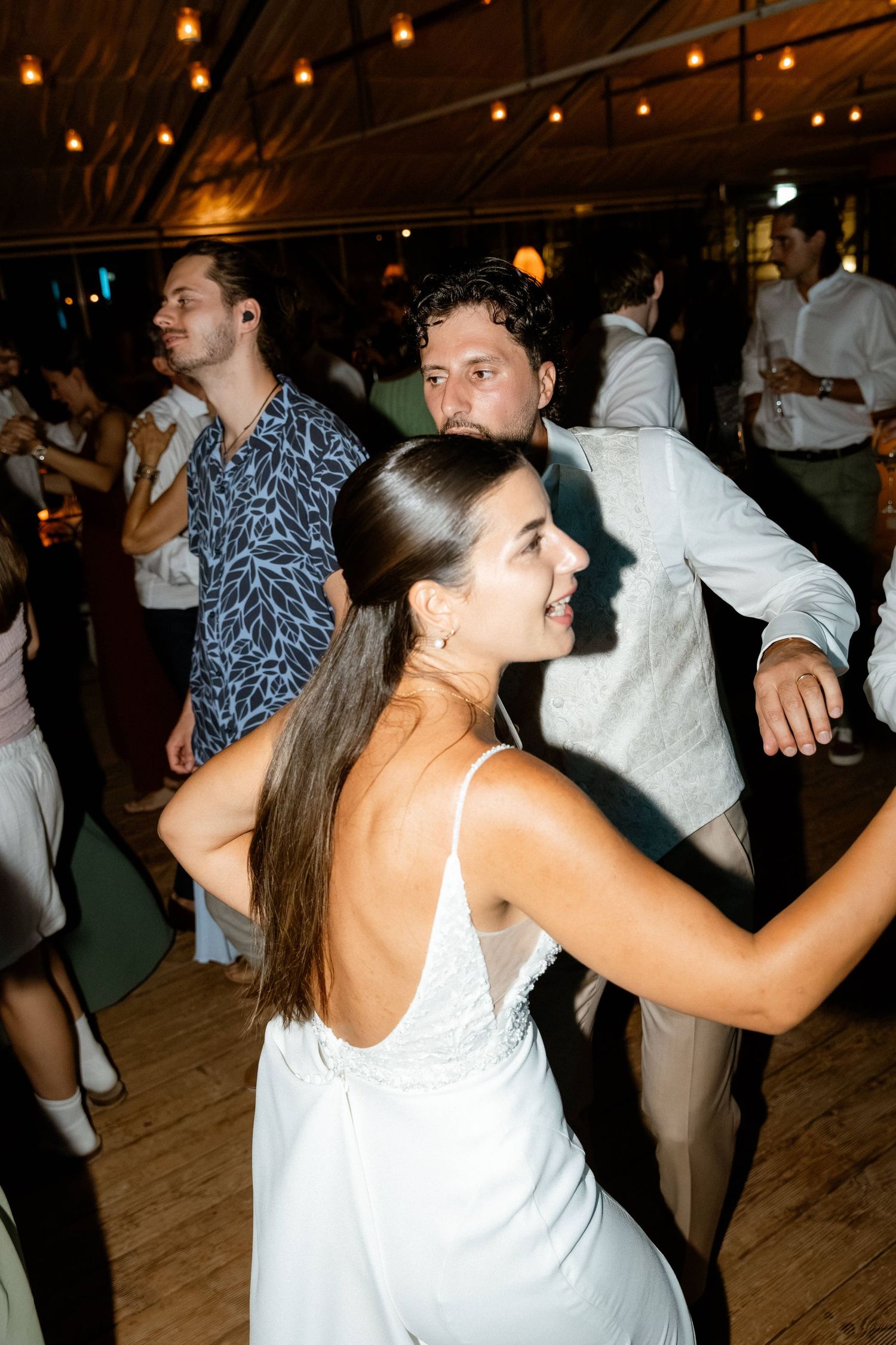 Bride in white dress dancing with guests at an indoor wedding reception.