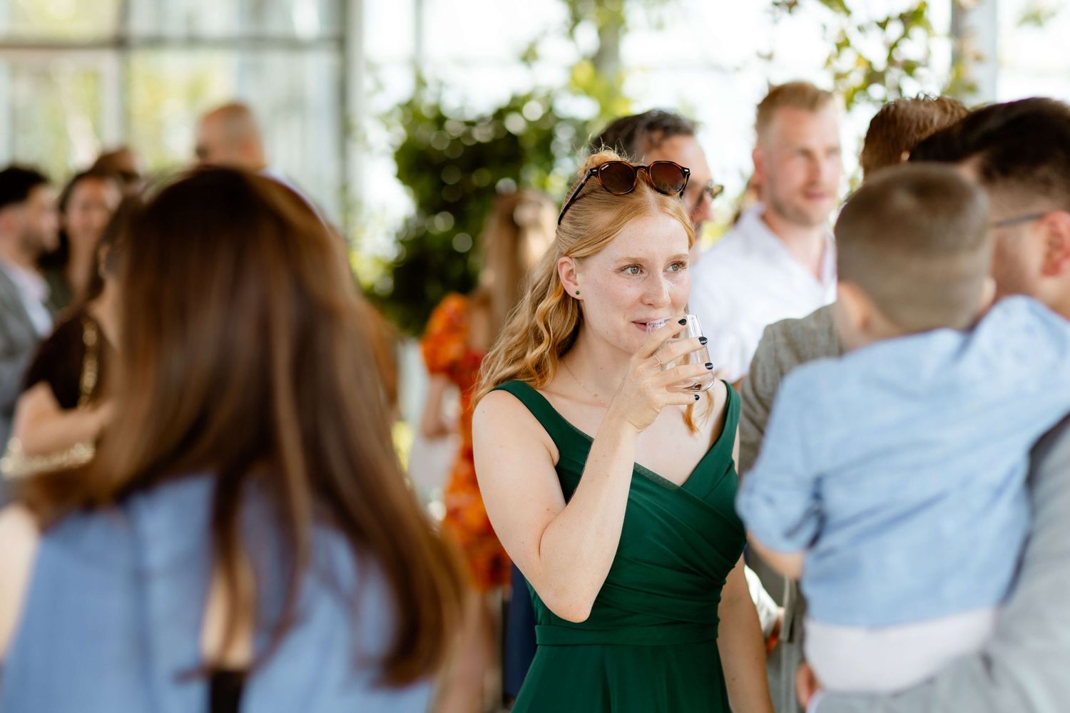 Woman in green dress smiling and chatting with guests at an outdoor wedding reception.