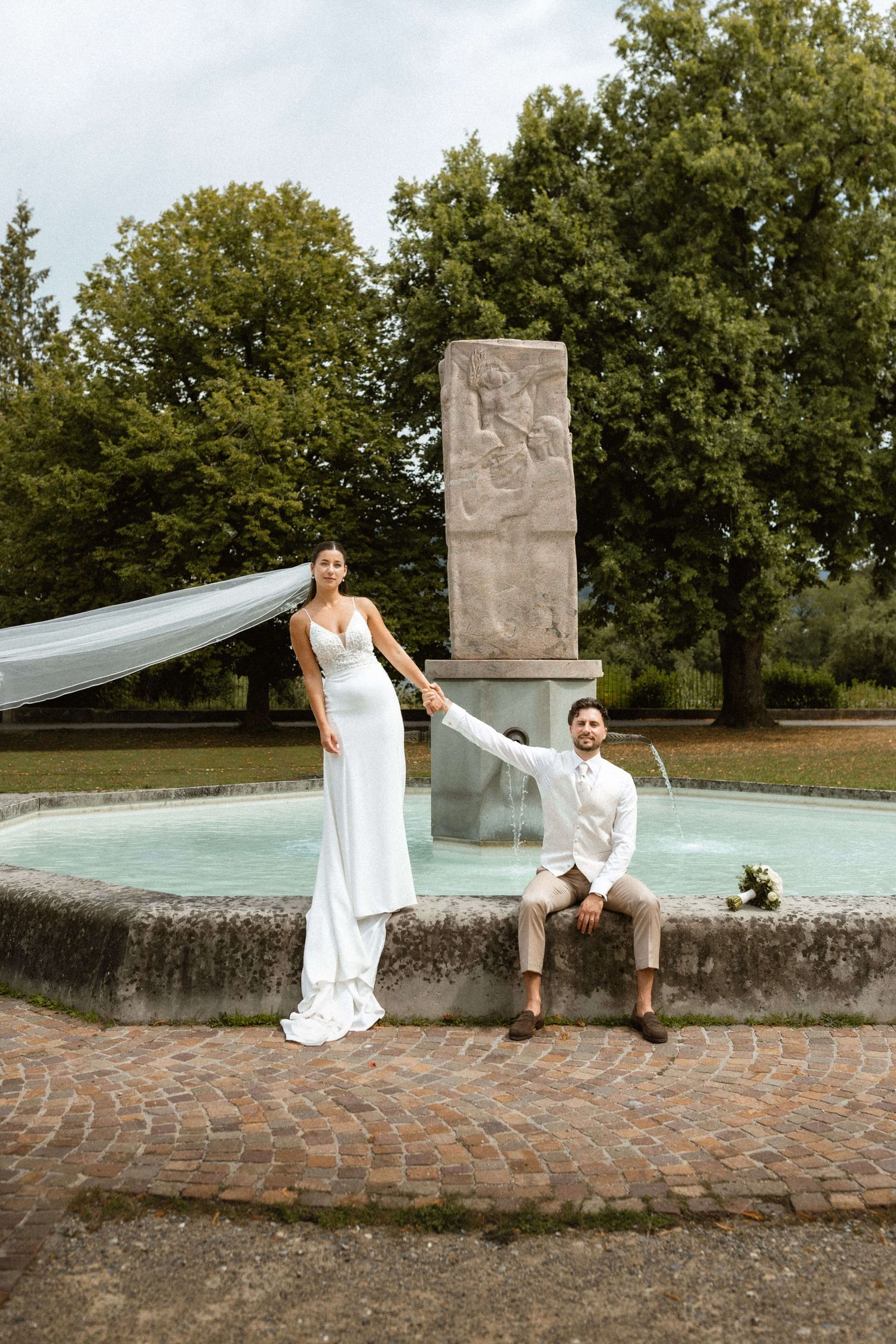 Brautpaar Hand in Hand an einem Brunnen bei einer Hochzeit in Vorarlberg.