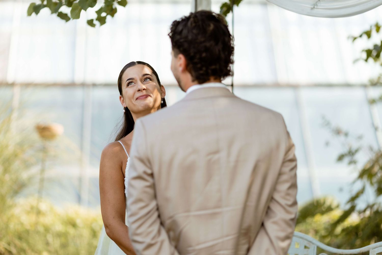 Bride in white dress gazes up at groom in tan suit during intimate wedding ceremony.