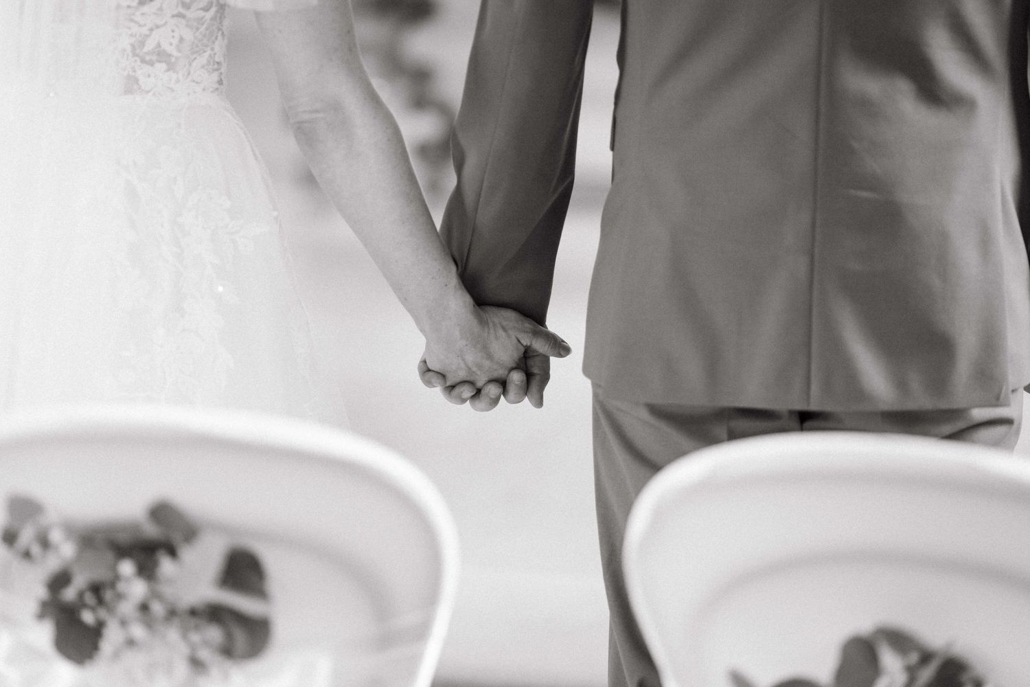 Black and white photo of bride and groom holding hands during wedding ceremony.