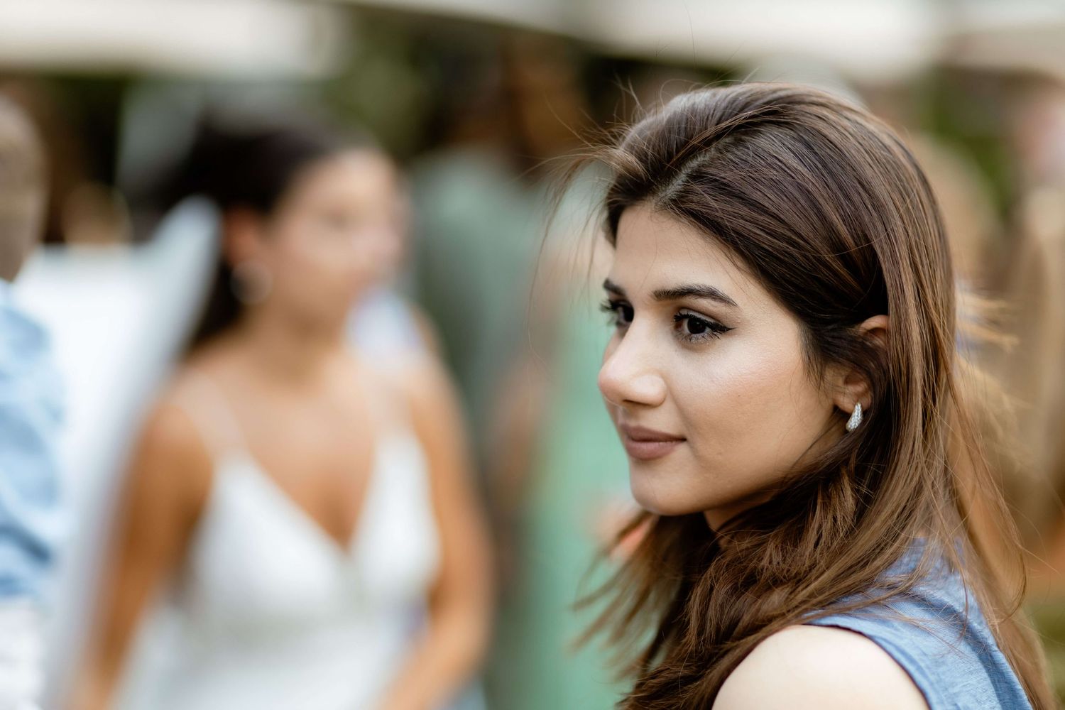Young brunette woman in blue dress gazes sideways at outdoor wedding reception.