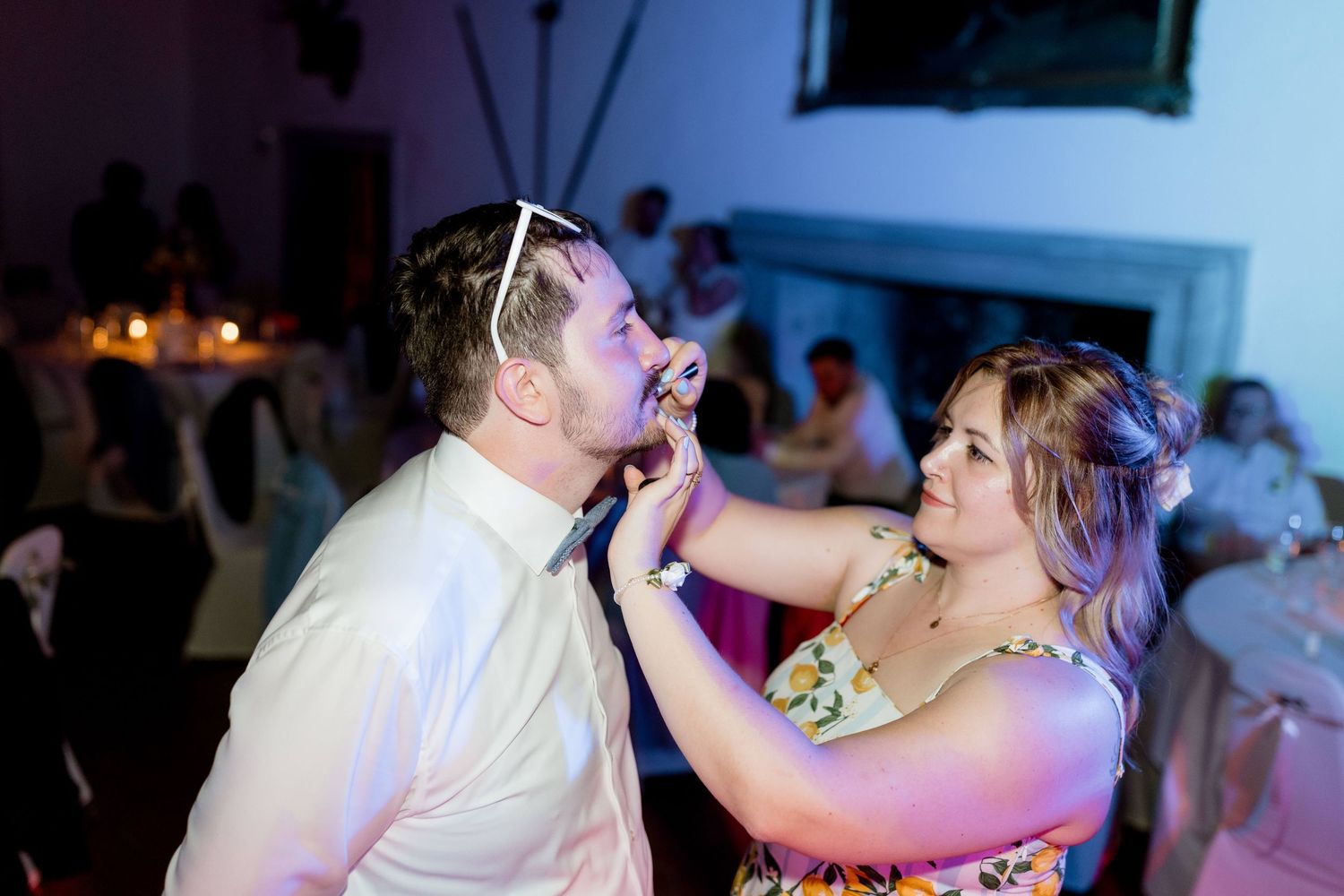 A woman playfully feeds a man in sunglasses at a candlelit wedding reception celebration.
