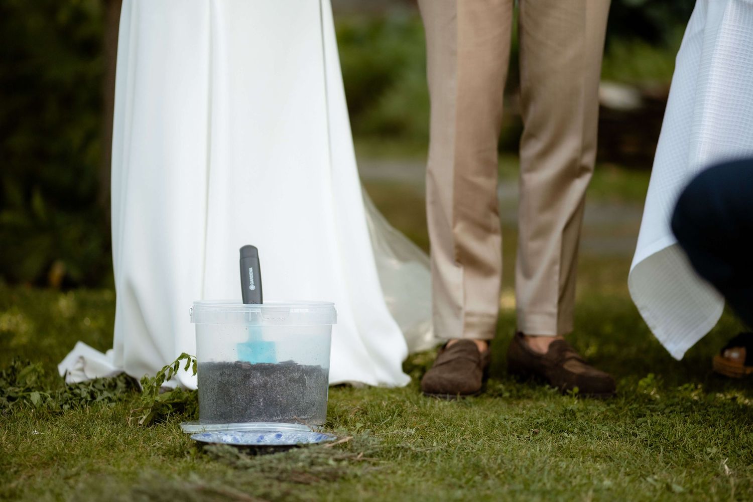 Couple standing on grass during wedding ceremony with a decorative sand unity bucket nearby.