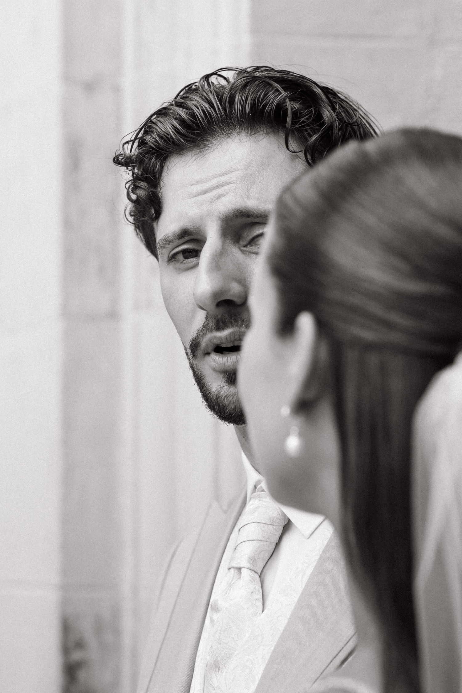 Black and white portrait of a groom in a suit gazing intently at his bride during wedding.