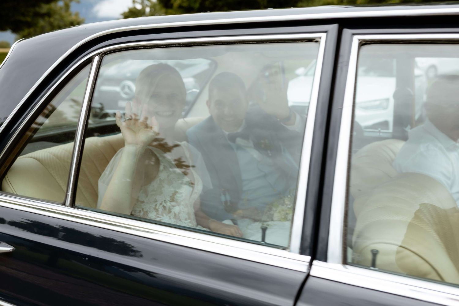 Bride waves from luxury wedding car window after church ceremony on wedding day.