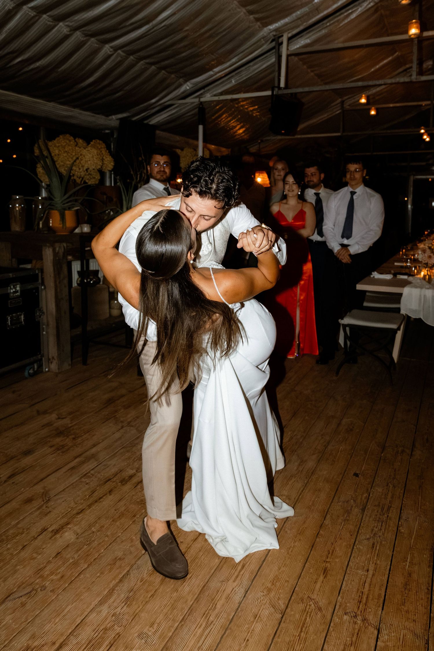 Groom dipping bride in white wedding gown during first dance at rustic wedding reception.