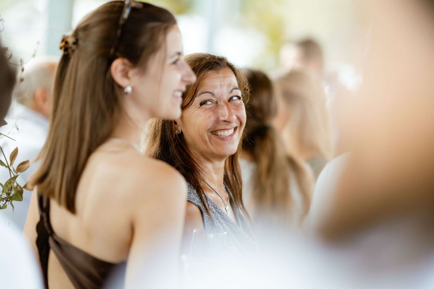 A smiling older woman in a blue dress shares a happy moment with a younger brunette woman at an outdoor event.