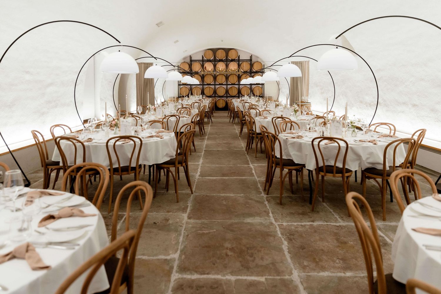 Elegant wedding reception venue with arched stone ceiling, round tables, and bentwood chairs.