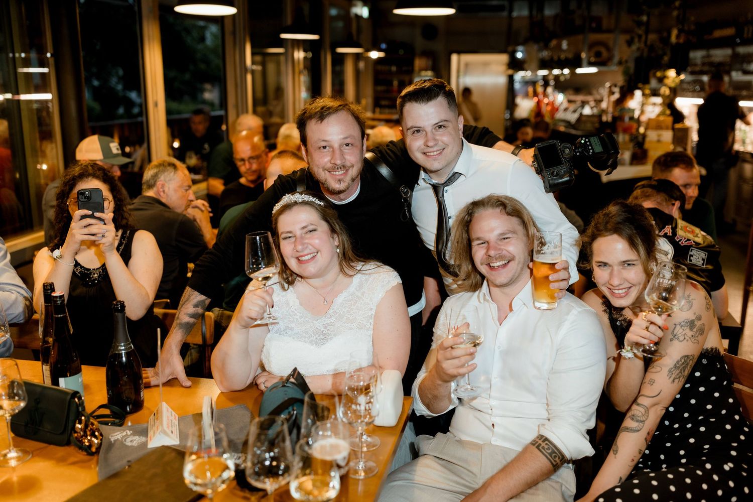 Group of friends celebrating at a wedding reception, raising glasses and smiling at a bar.