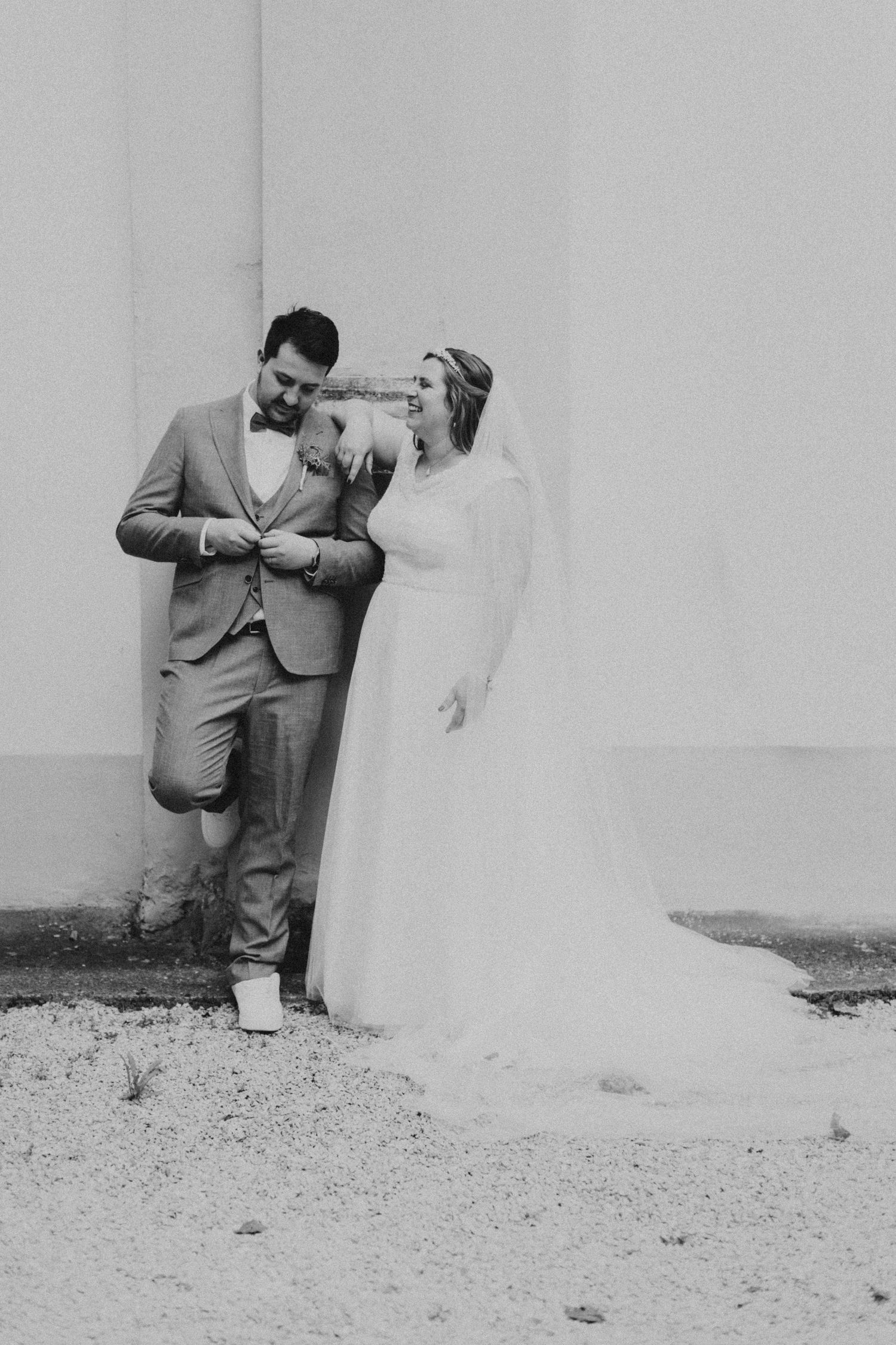 Black and white portrait of bride and groom sharing a tender moment against a white wall.
