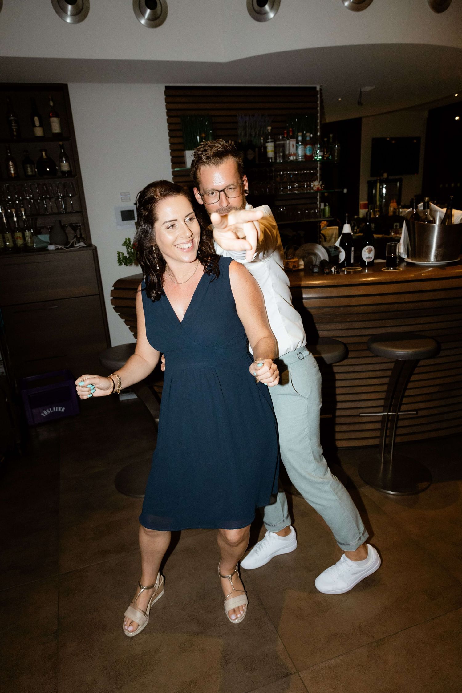 Couple dancing joyfully with a child at a wedding reception near a bar.