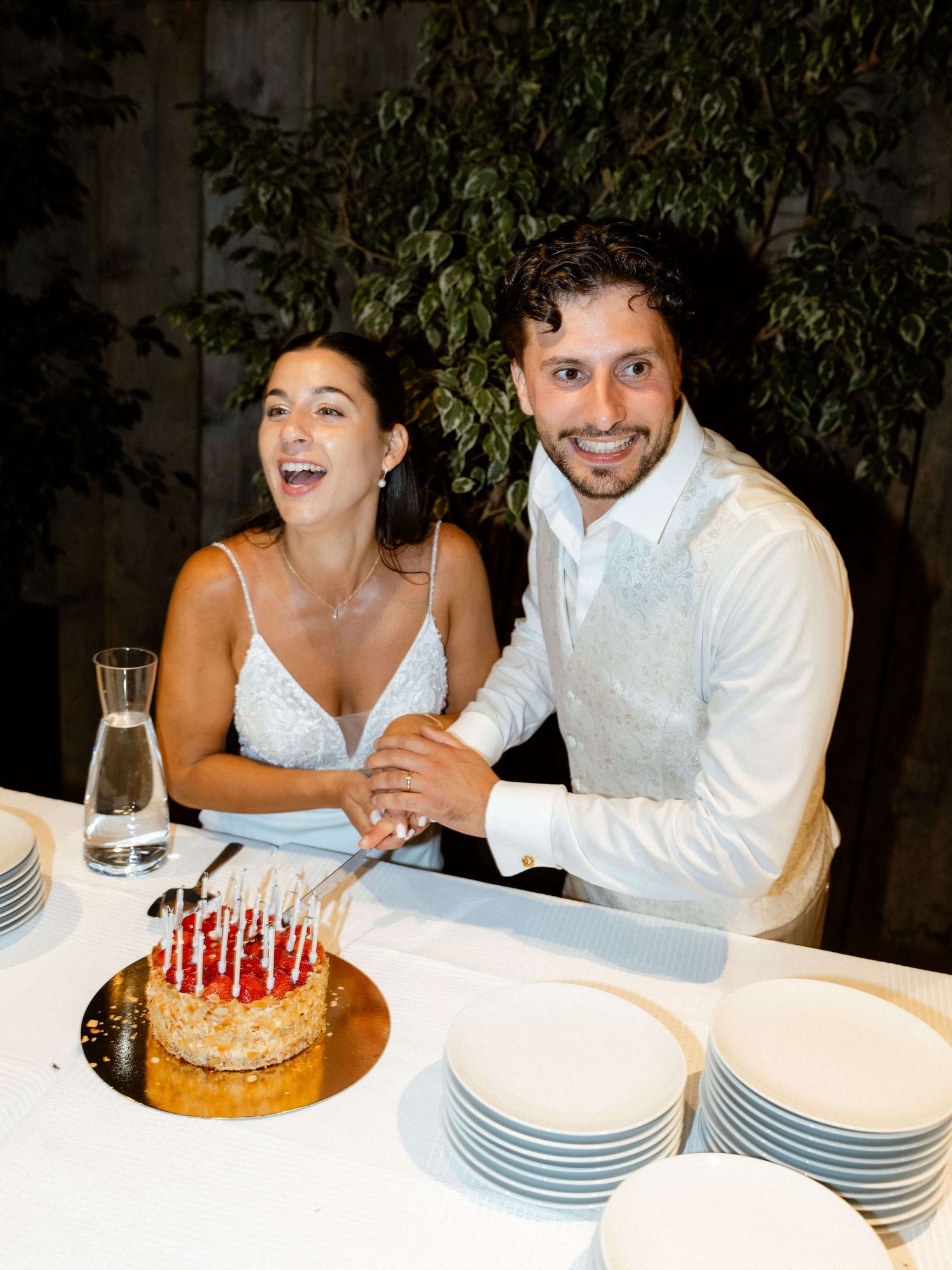 Smiling bride and groom posing together while cutting their wedding cake.