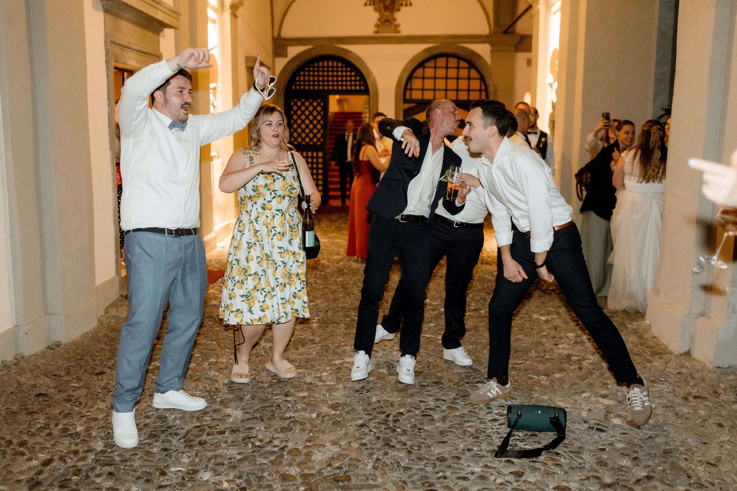 Wedding guests dance and celebrate joyfully in an elegant Italian courtyard with arched architecture.