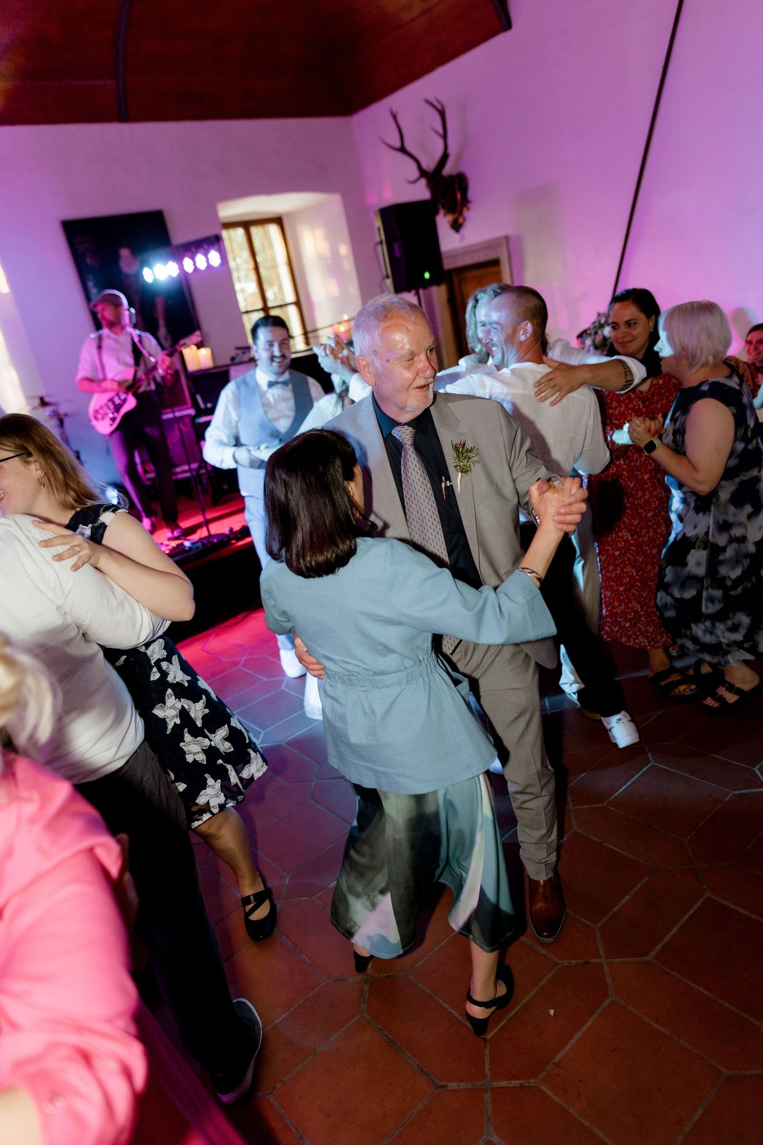 Wedding guests dance energetically on a colorful dance floor with a live band performing in the background.