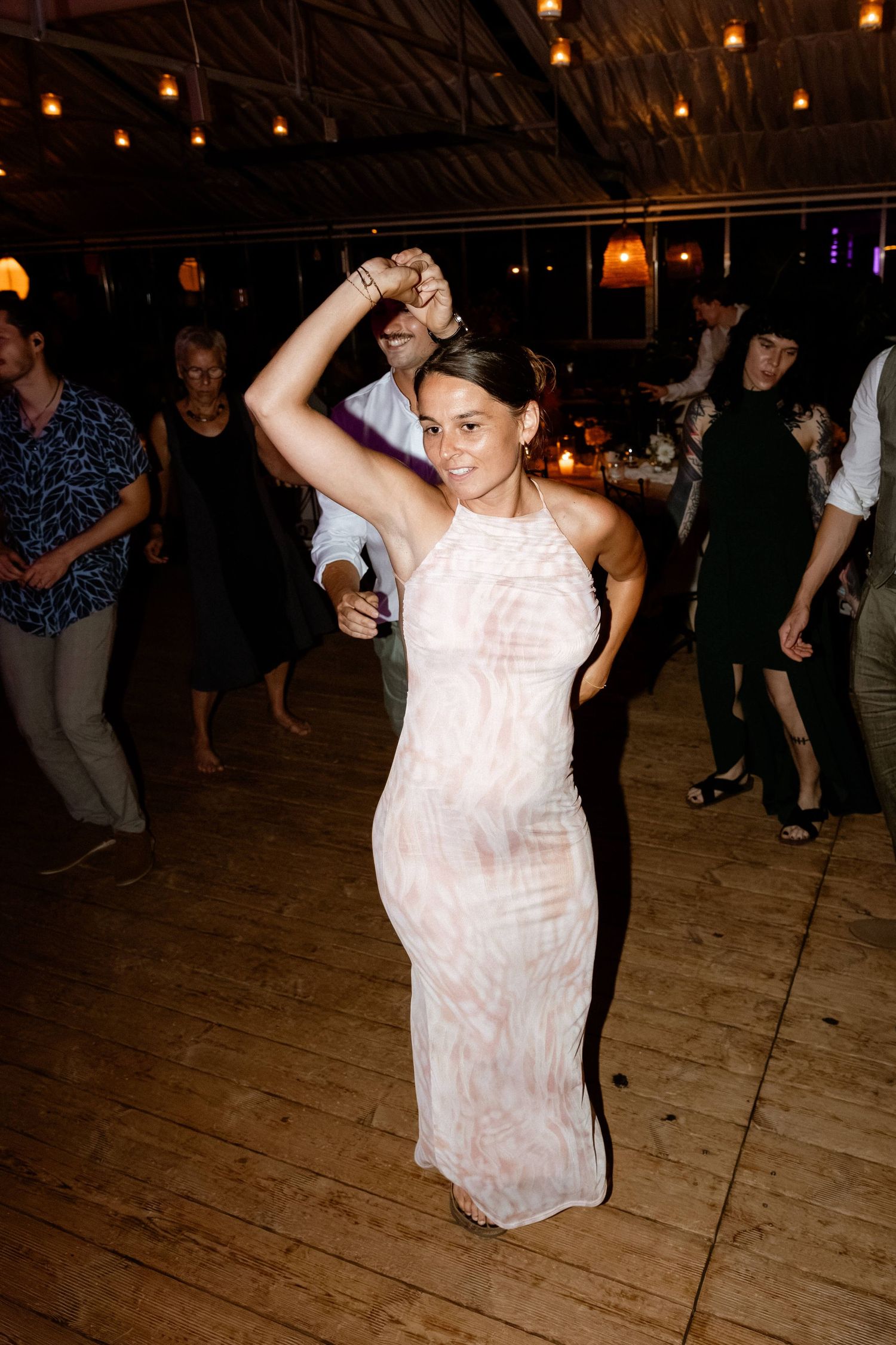 Guest in floral maxi dress dancing joyfully at wedding reception on wooden dance floor.