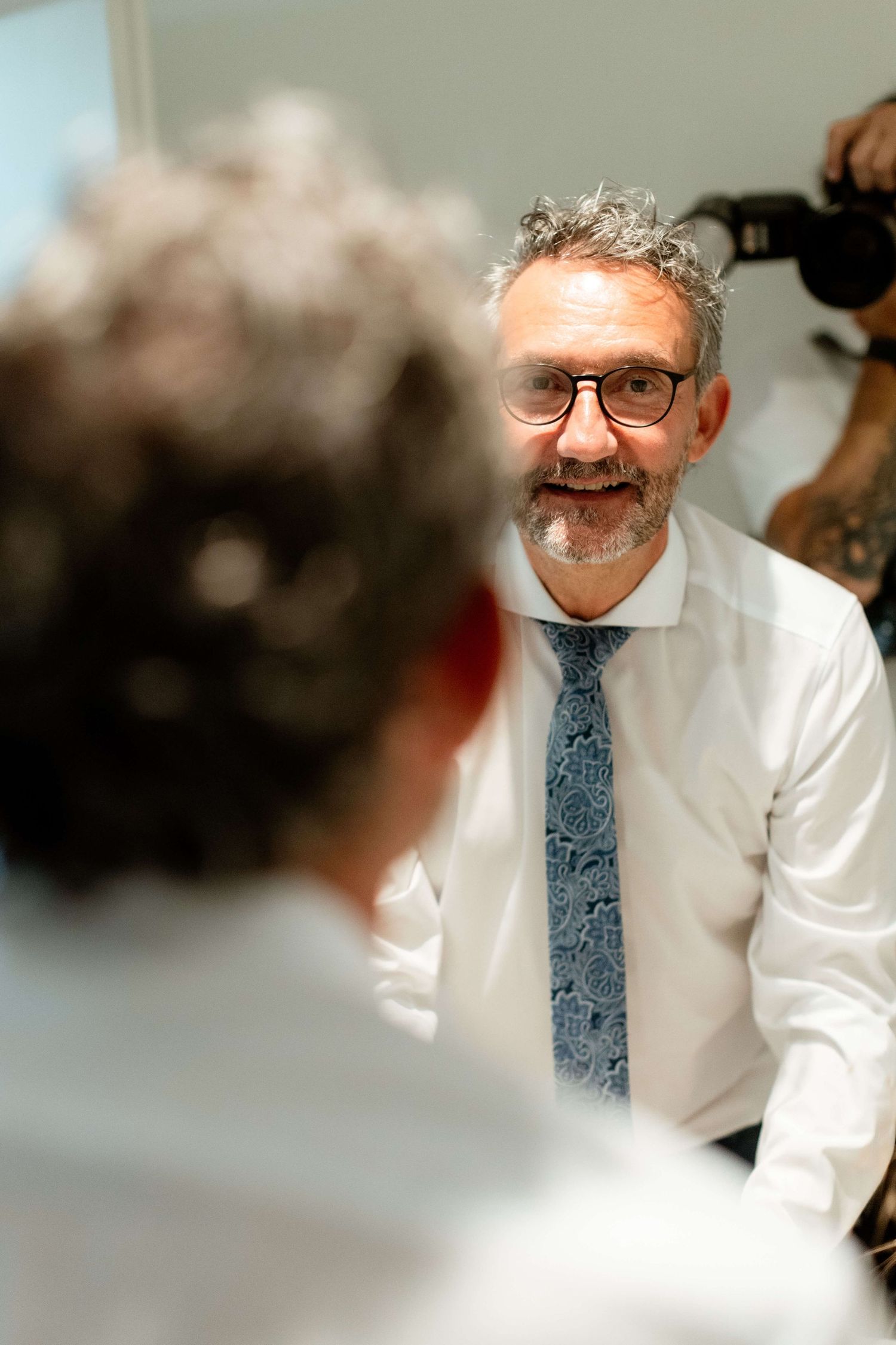 Smiling middle-aged man with glasses and floral tie at a wedding celebration.