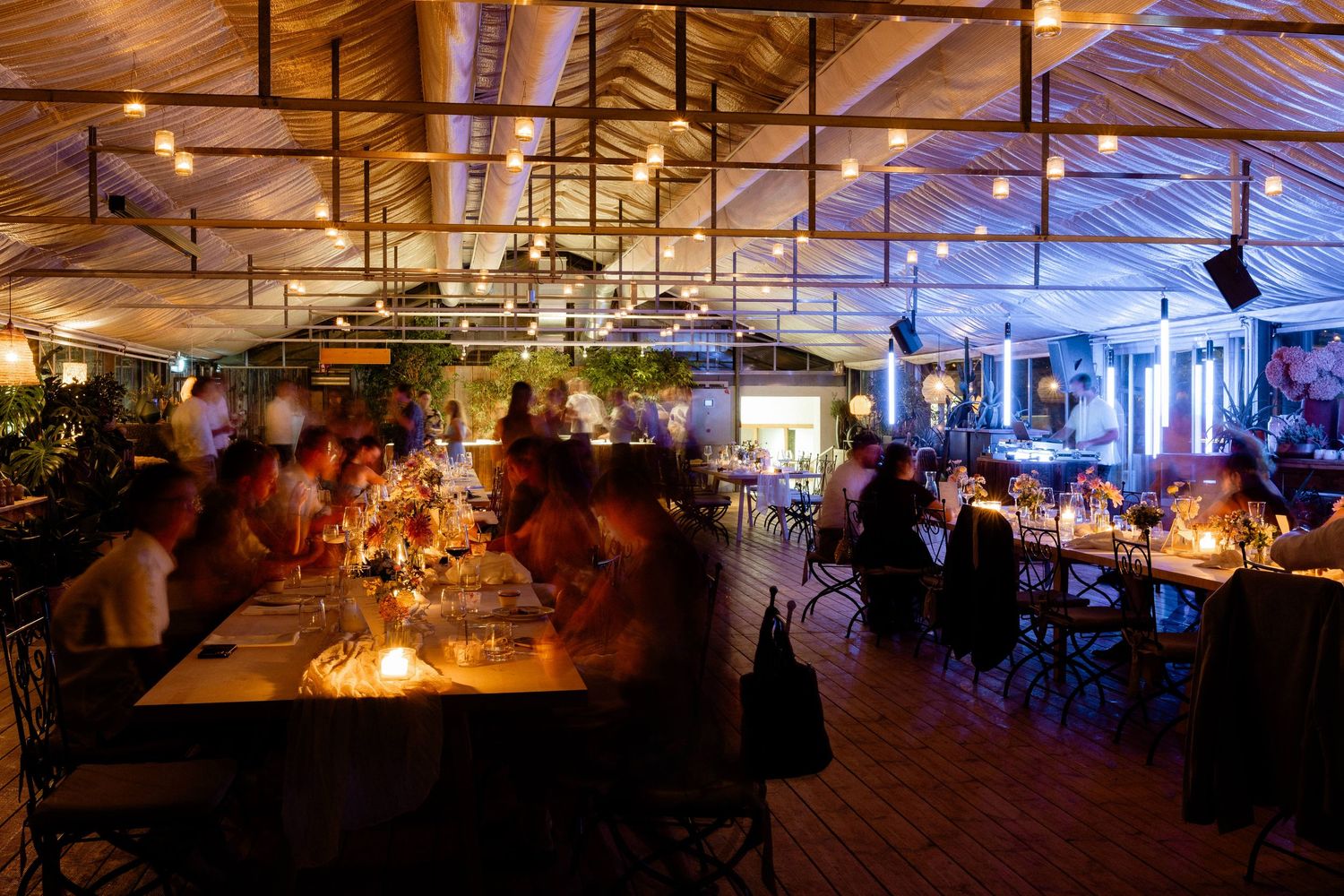 Elegant wedding reception dinner in warmly lit rustic venue with long candlelit tables.