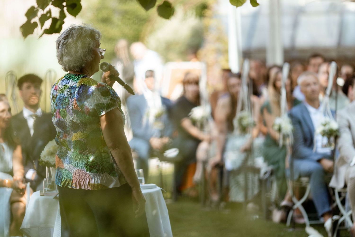 Wedding officiant addresses seated guests during an elegant outdoor garden ceremony.
