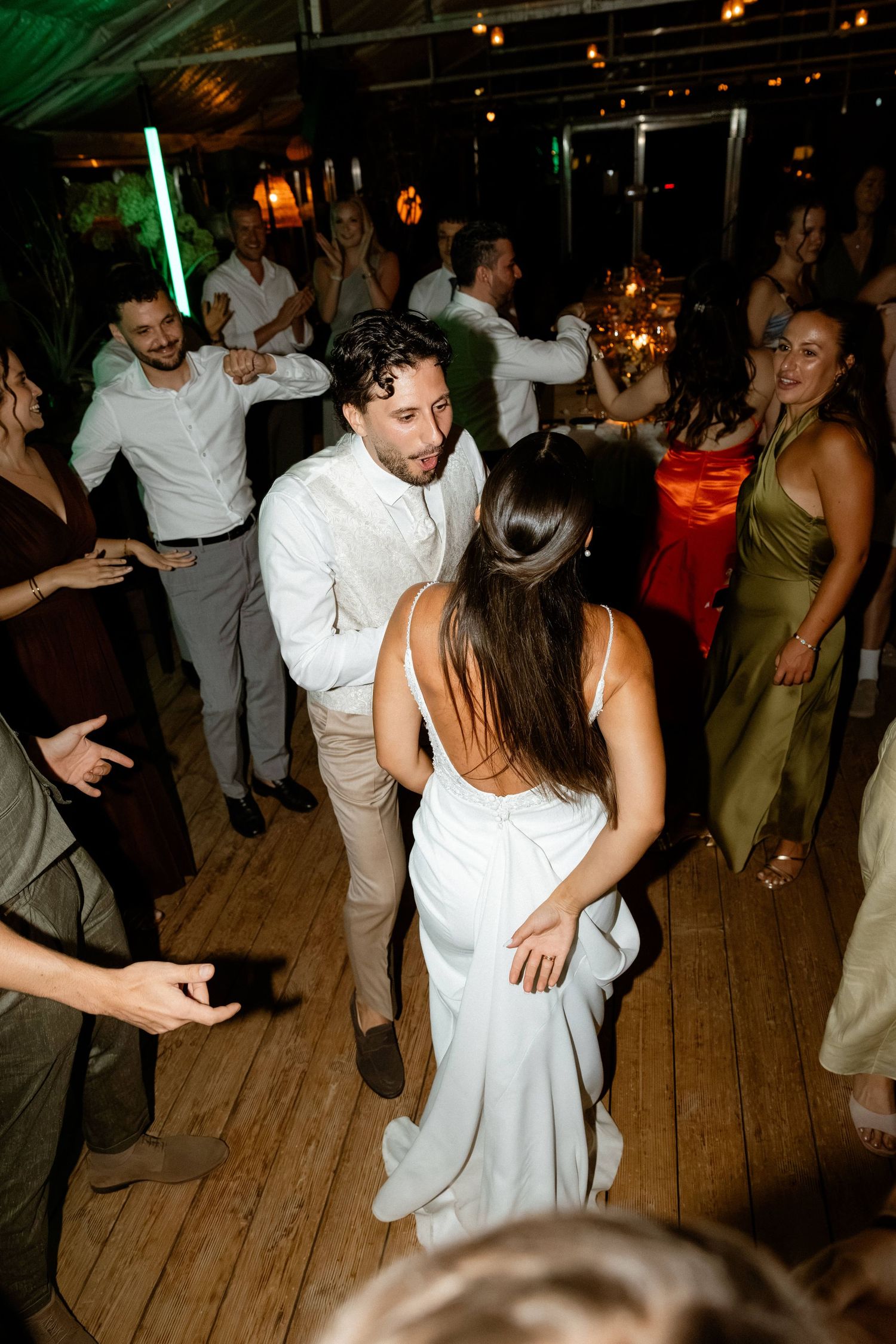 Bride and groom sharing a dance surrounded by celebrating guests on the wedding reception dance floor.