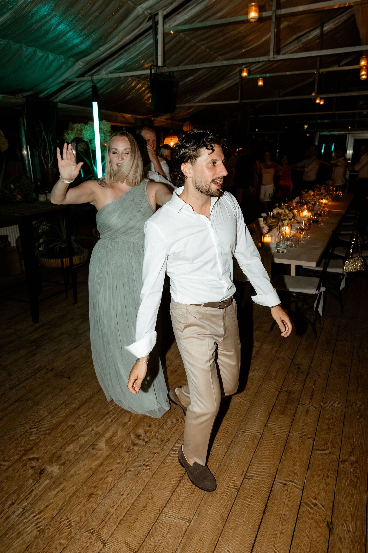 Man in white shirt and woman in sage bridesmaid gown dancing at wedding reception.