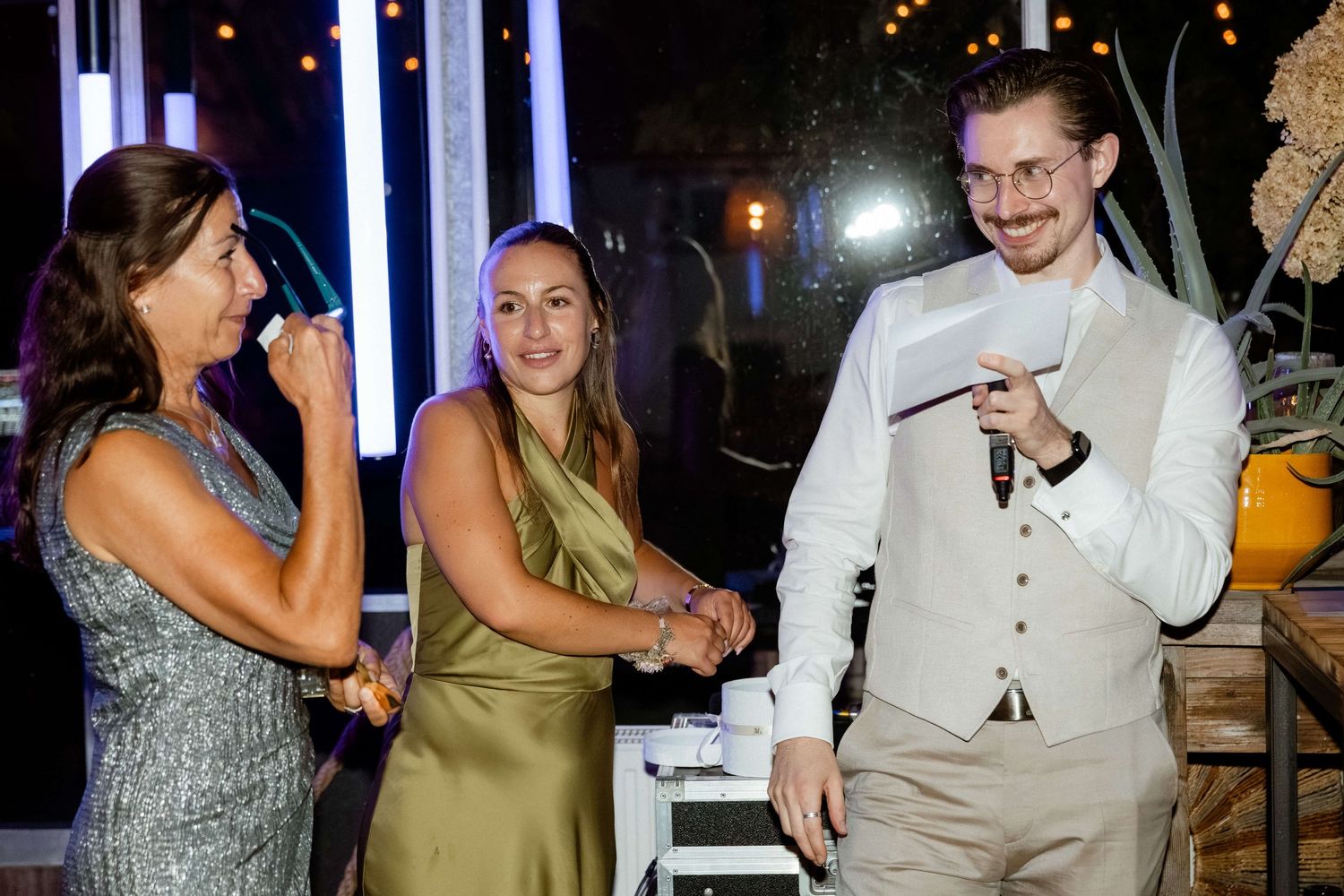 Wedding guests smiling and holding hands during fun reception activity indoors at night.