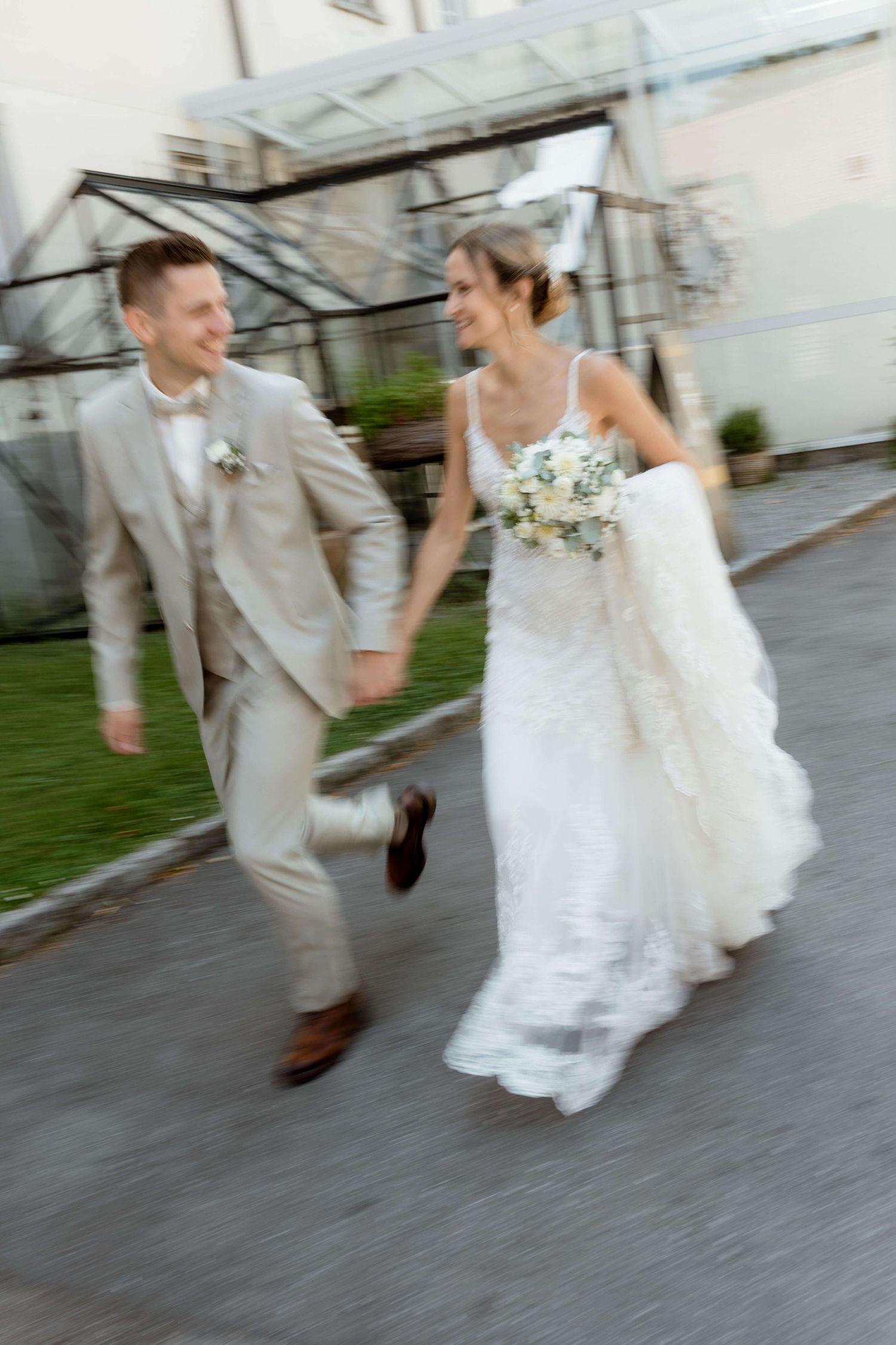 Joyful bride and groom run hand in hand, laughing, in a motion-blurred wedding photo.