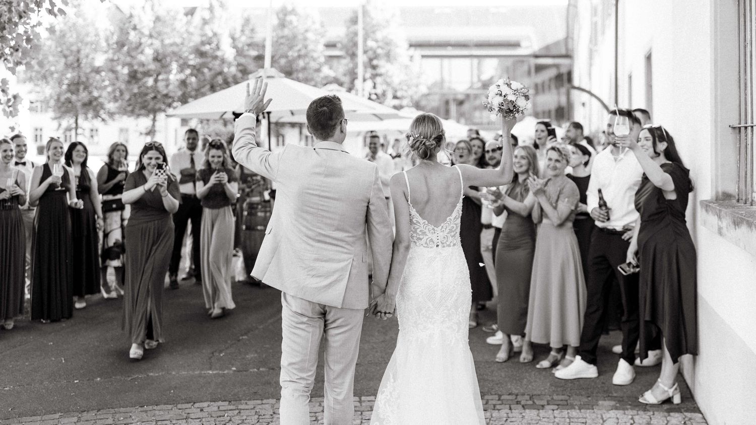 Bride and groom walking through a joyful crowd of wedding guests applauding them in black and white photo.