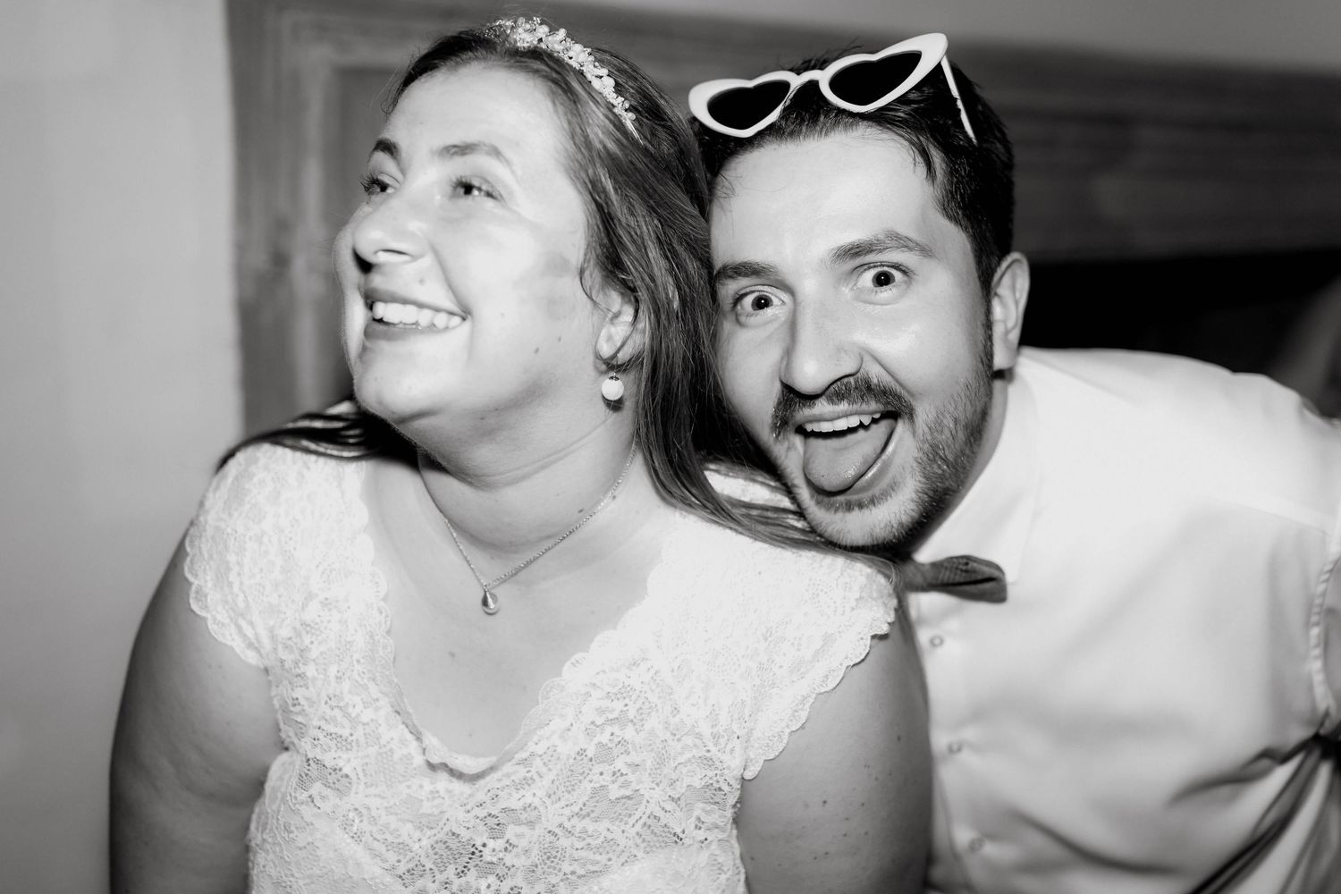 Black and white photo of smiling bride and groom making silly faces together at their wedding reception.