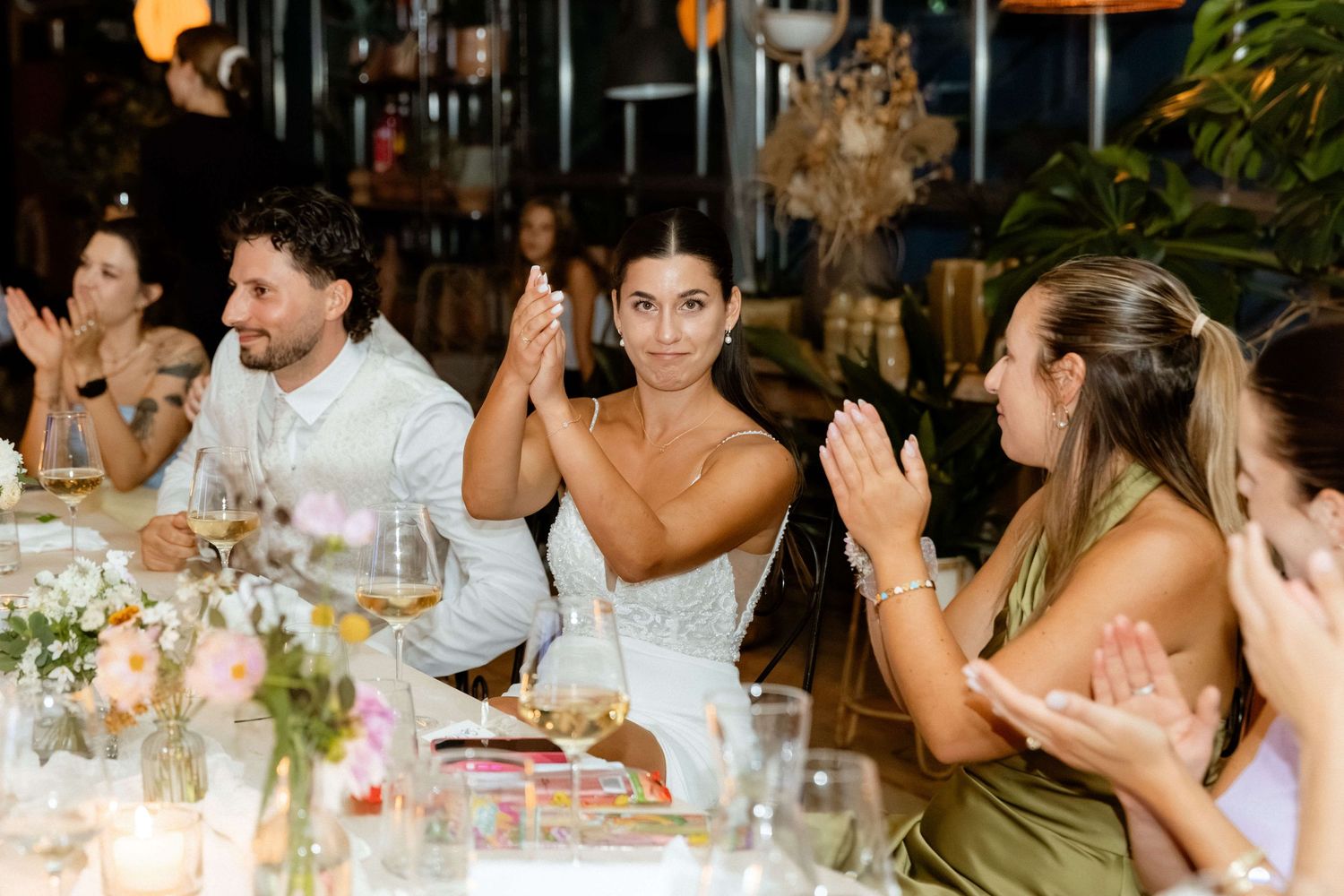 Wedding guests clapping and applauding at an elegant candlelit reception dinner table with floral centerpieces.